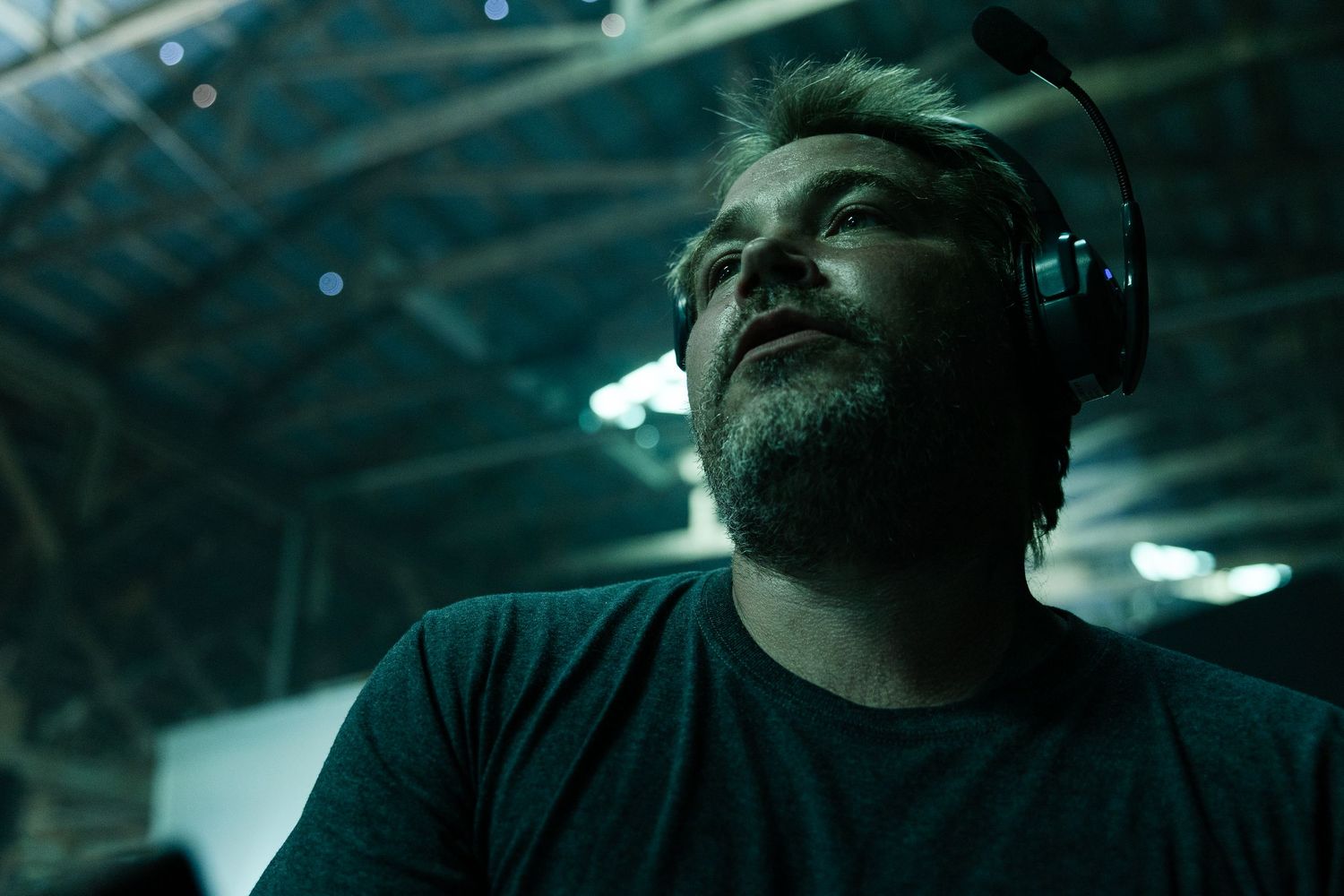 Individual wearing headphones gazes upward in a dark setting with teal lighting overhead.