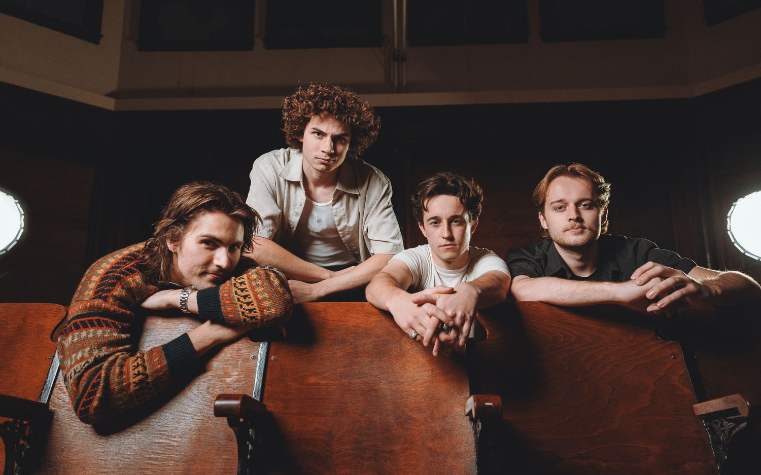 A group of four people leaning casually on a wooden surface in a dimly lit room.