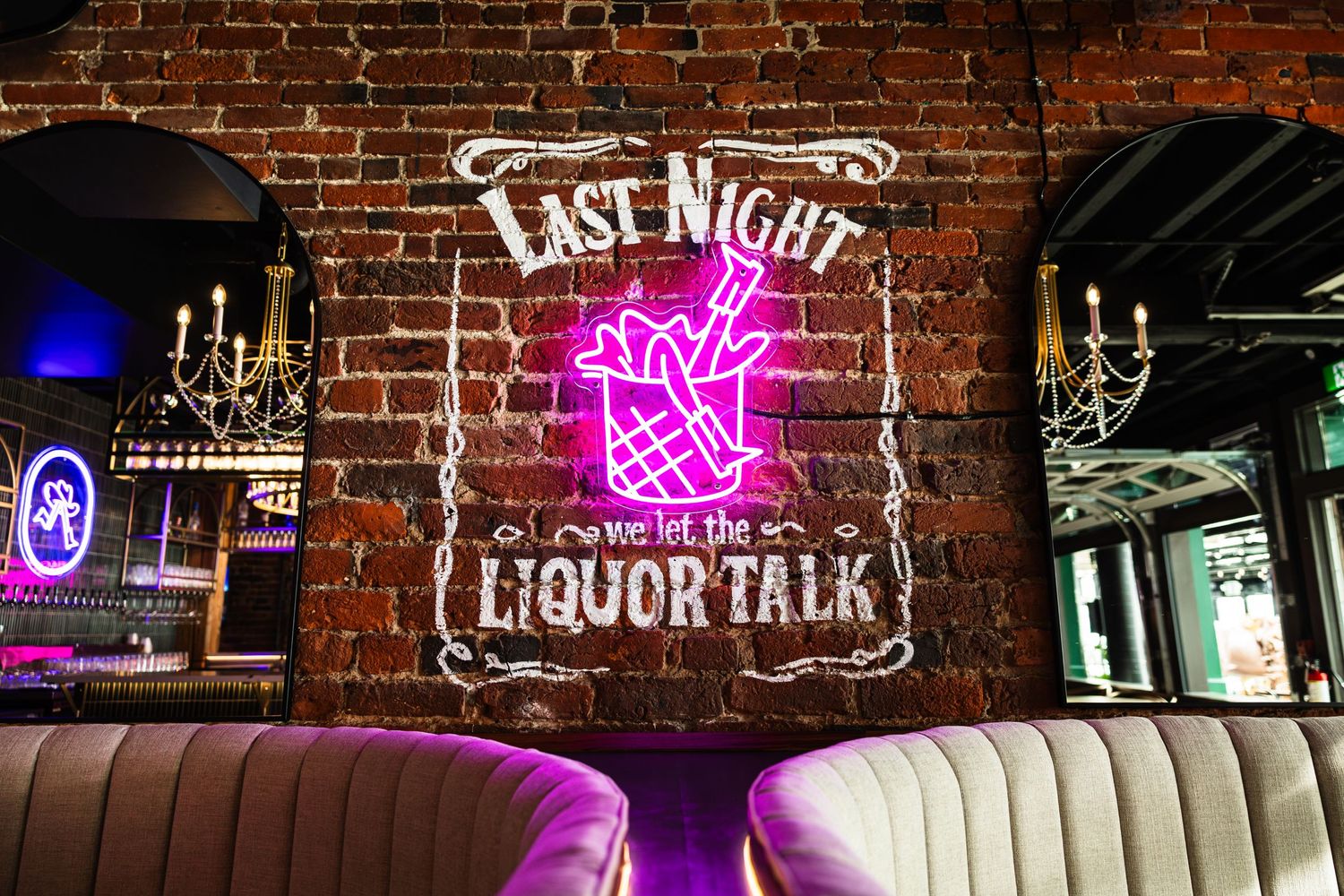Pink neon sign reading 'Last Night Liquor Talk' glows against exposed brick wall above leather booth seating.