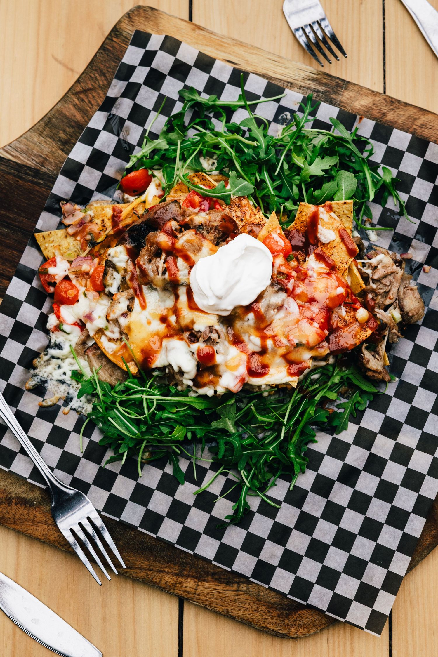 Gourmet loaded fries topped with sour cream and fresh arugula served on a checkered paper on wooden board.
