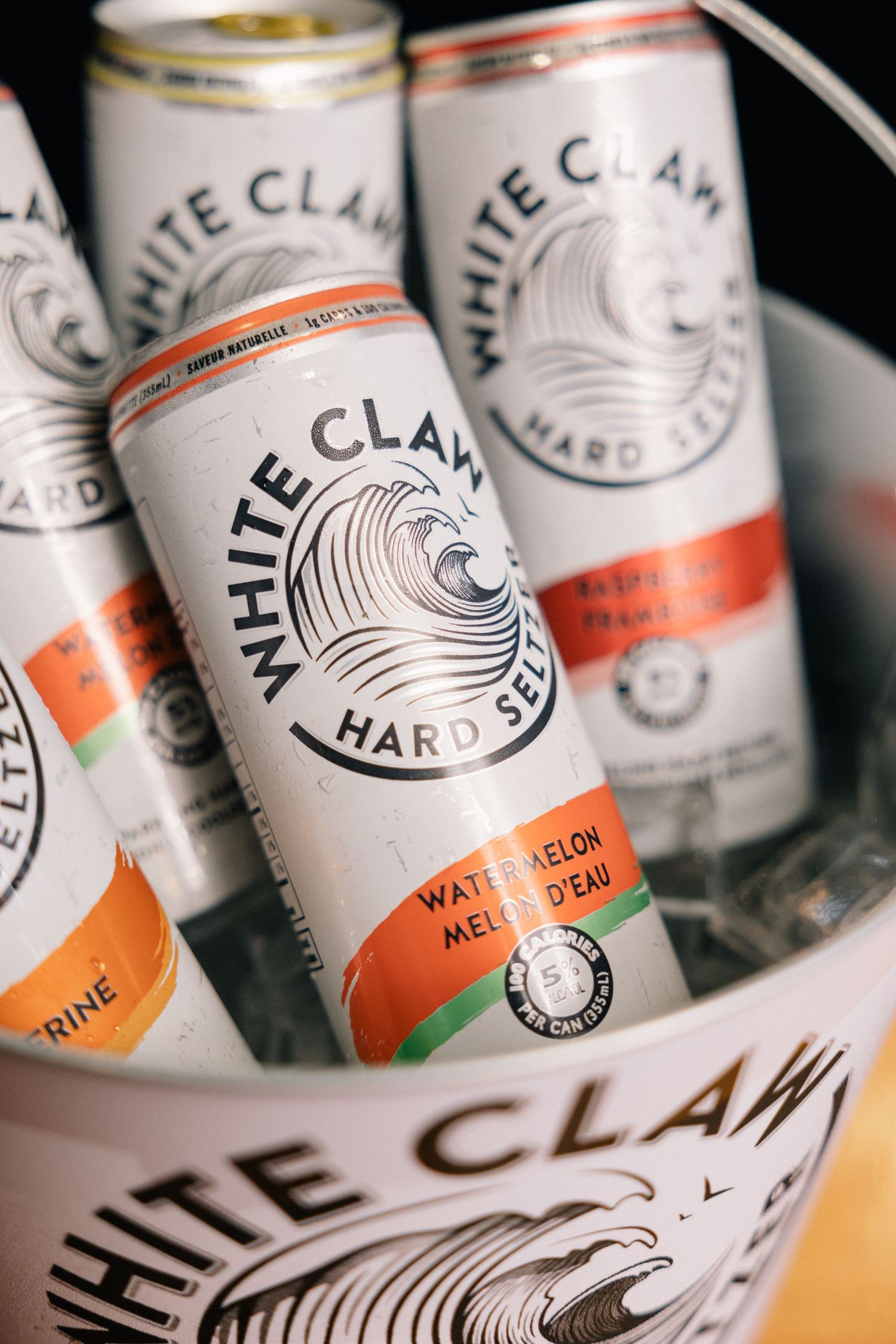 Multiple cans of White Claw Hard Seltzer in Watermelon flavor shown on ice with black and orange branding.