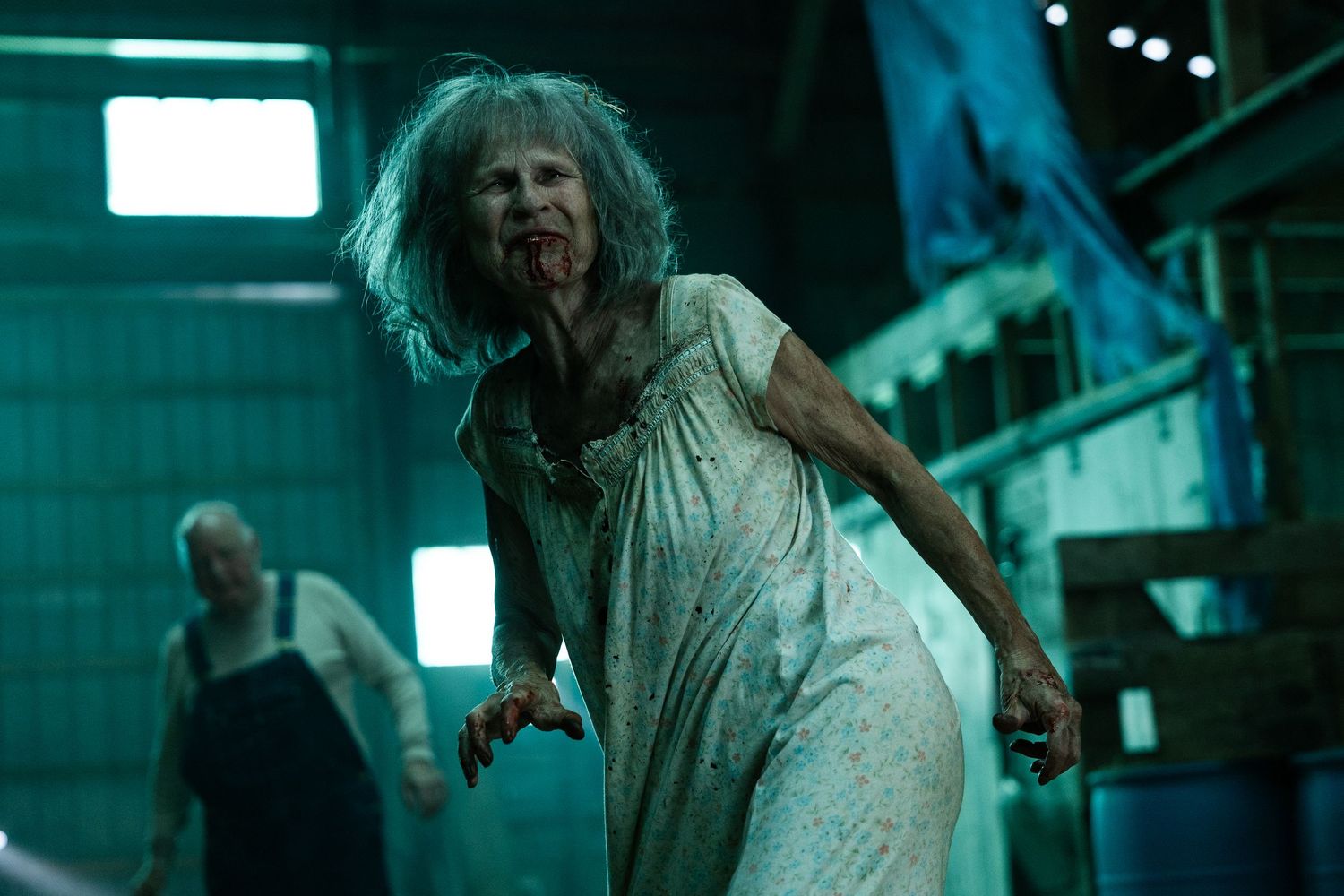 A zombie-like figure in a blood-stained white gown stands menacingly in a dimly lit industrial setting.