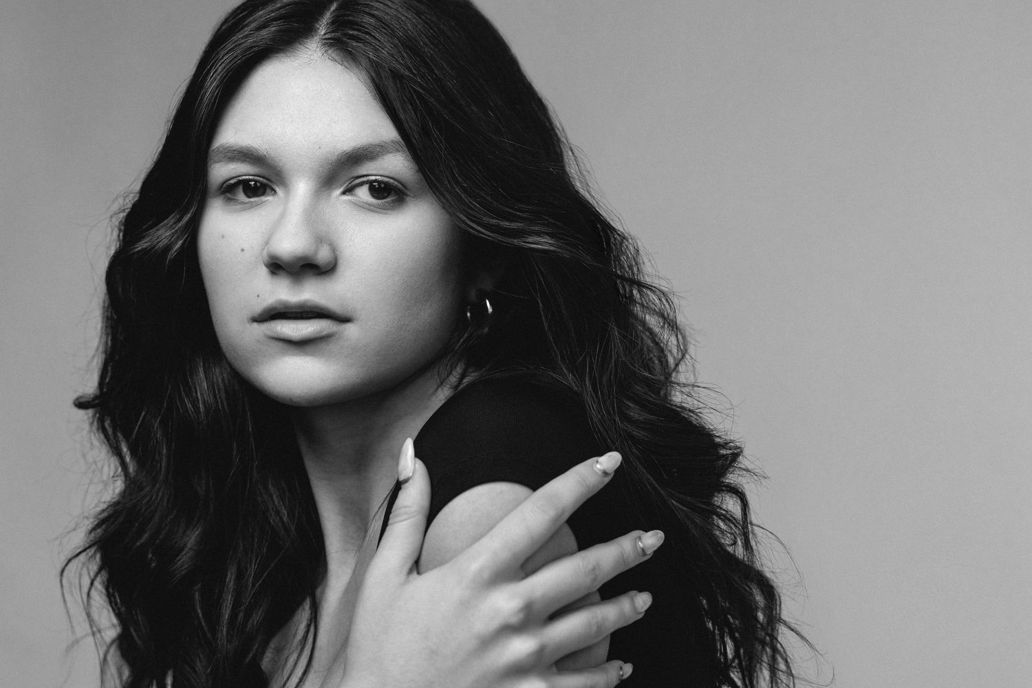 Black and white portrait series showing a figure with dark wavy hair in various elegant poses against a white background.