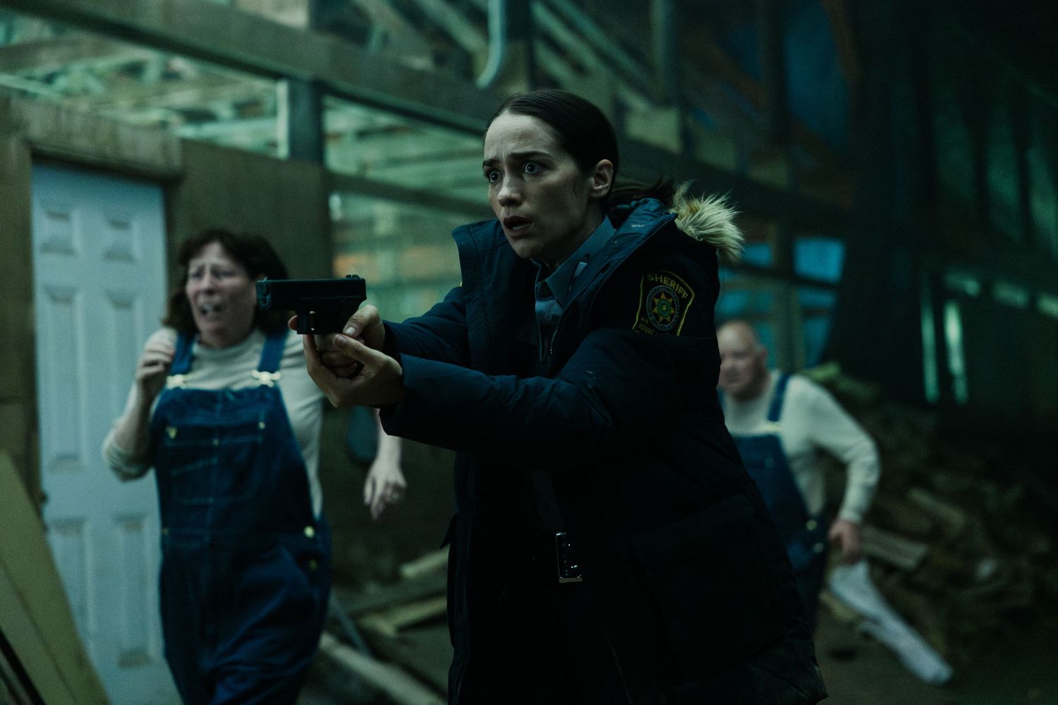 Person in a police uniform with a gun drawn stands alert in a darkly lit industrial or urban setting.