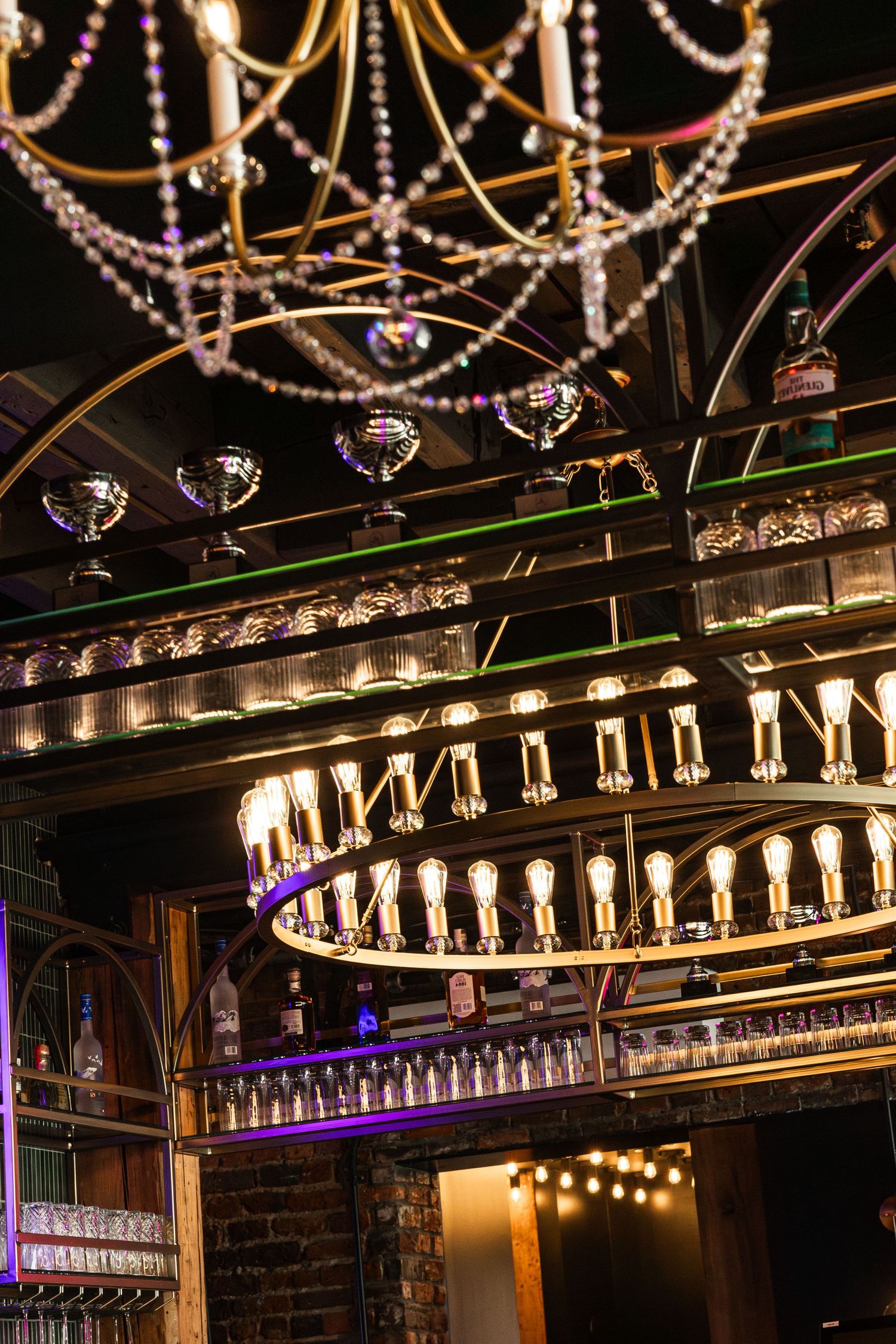 Elegant chandelier and lighting fixtures with crystal beads illuminate a vintage-style bar interior with warm ambiance.
