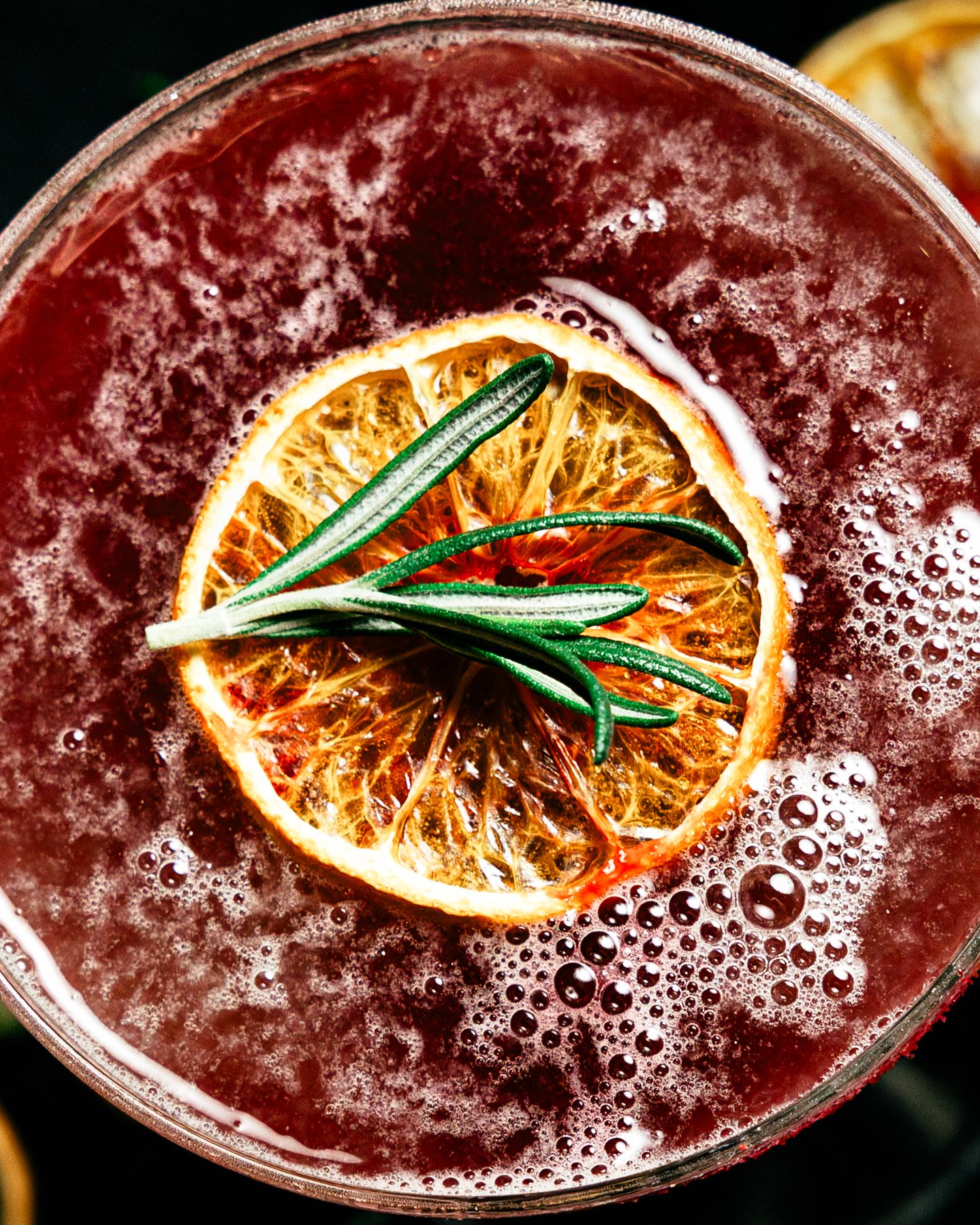 Overhead view of red cocktail garnished with dehydrated orange slice and fresh rosemary.