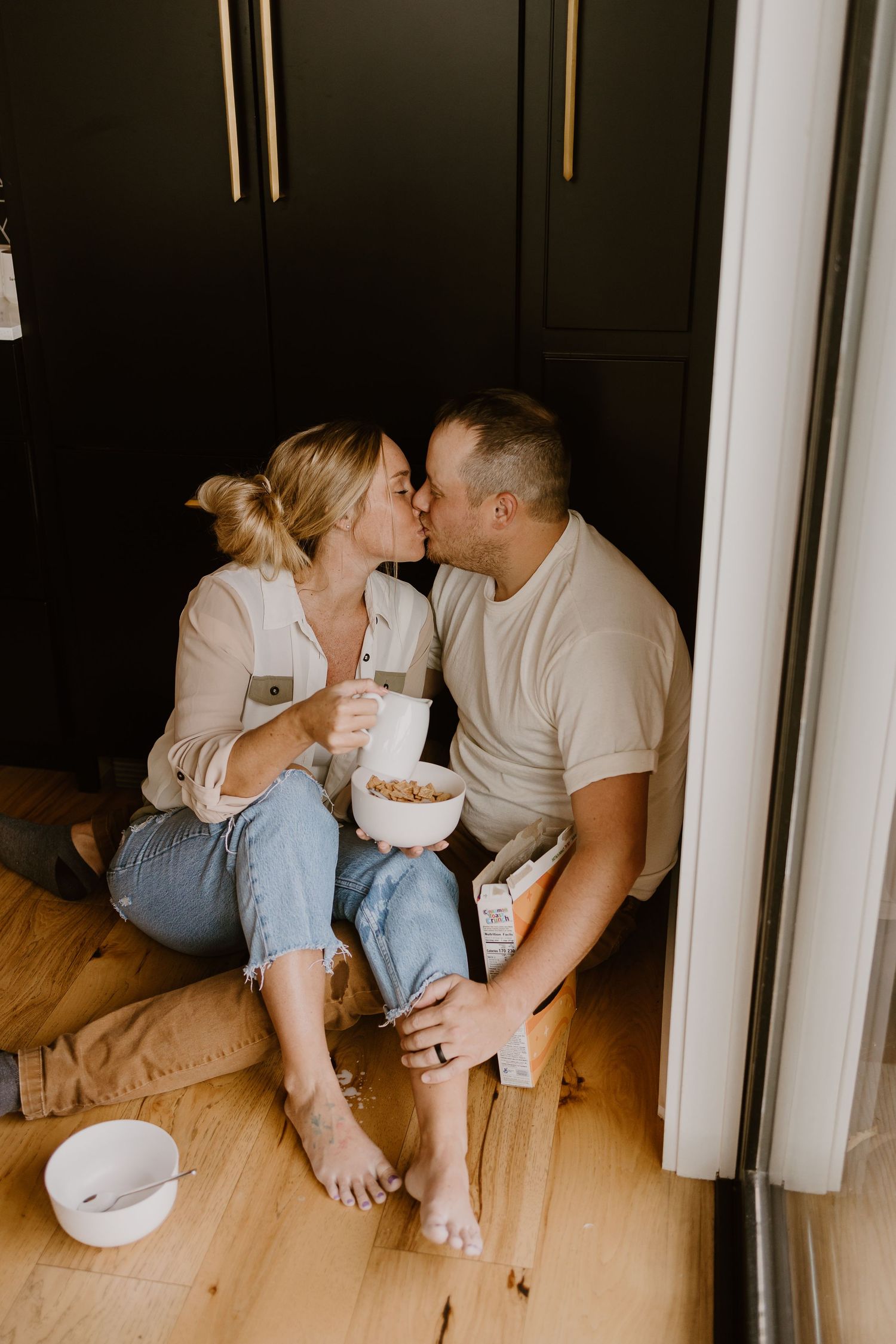 A romantic couple sits on a wooden floor sharing snacks and intimate moments in a cozy indoor setting.