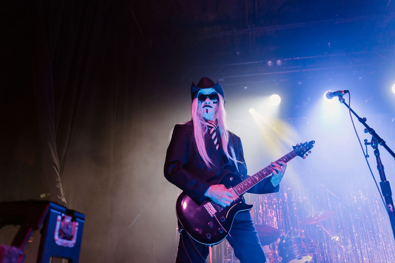 Musicians performing with guitars under blue stage lighting and atmospheric effects.