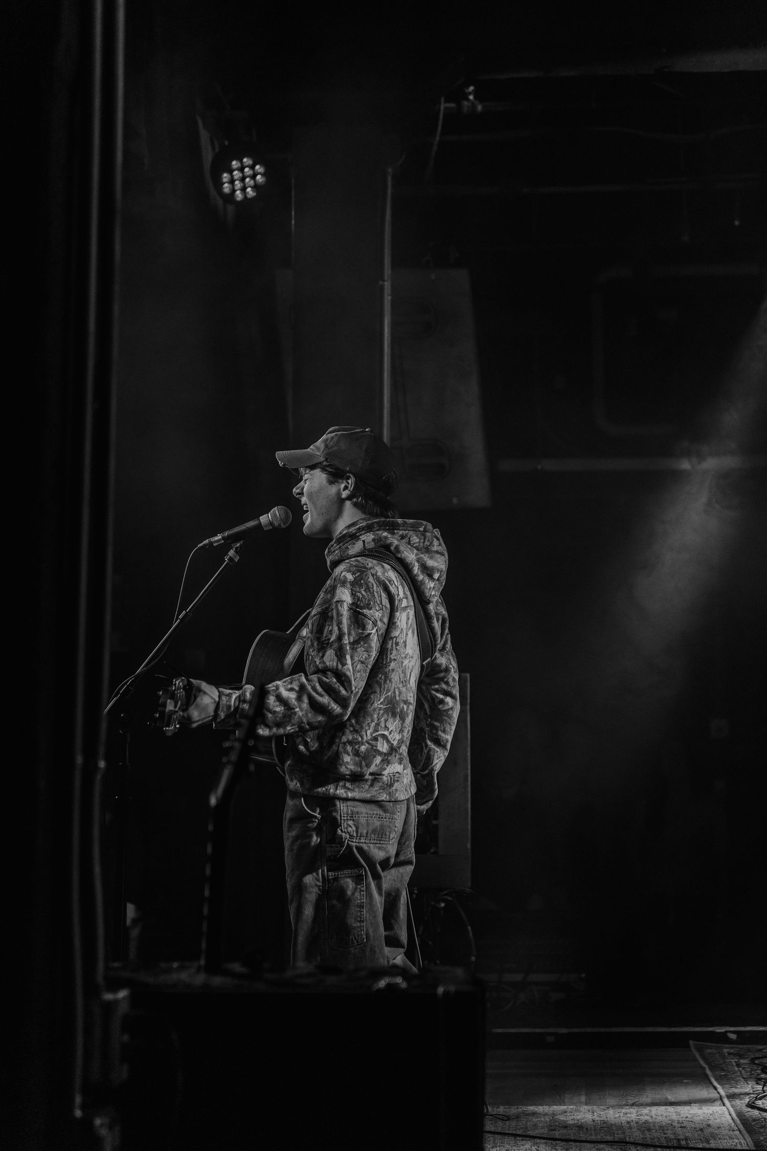 Black and white photo of musician performing on dimly lit stage.
