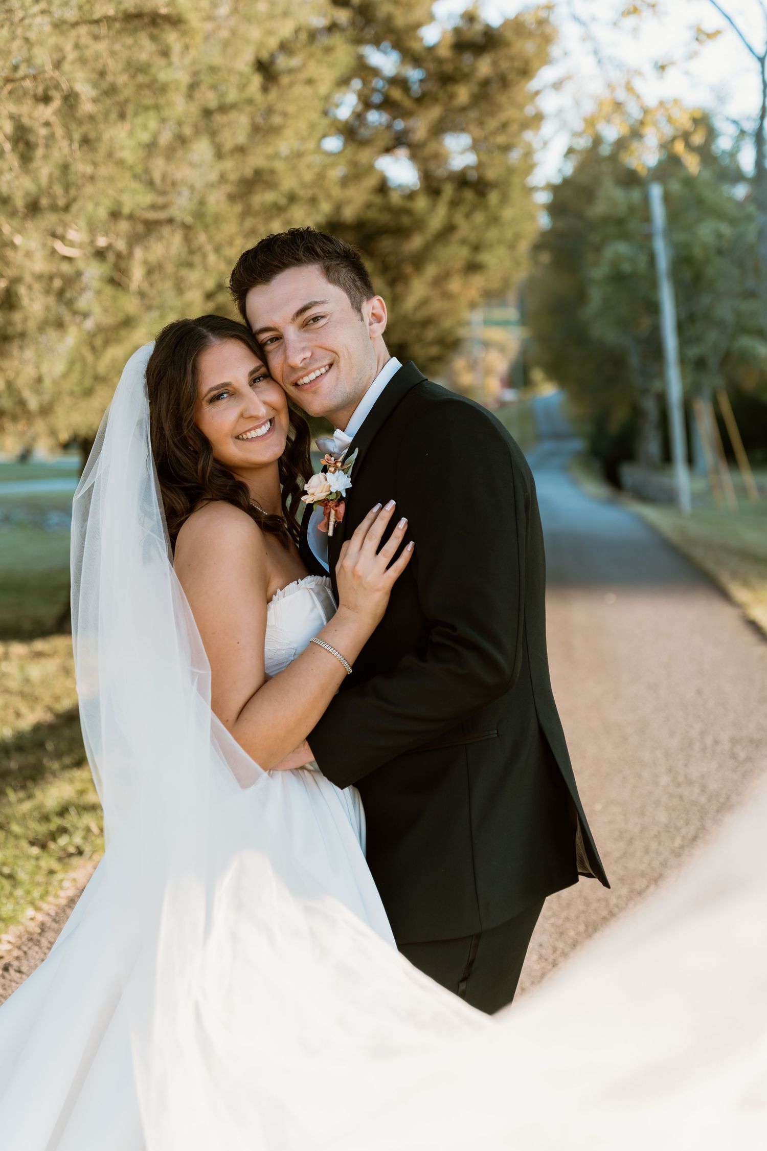 Romantic wedding photos of couple on tree-lined path during fall season.