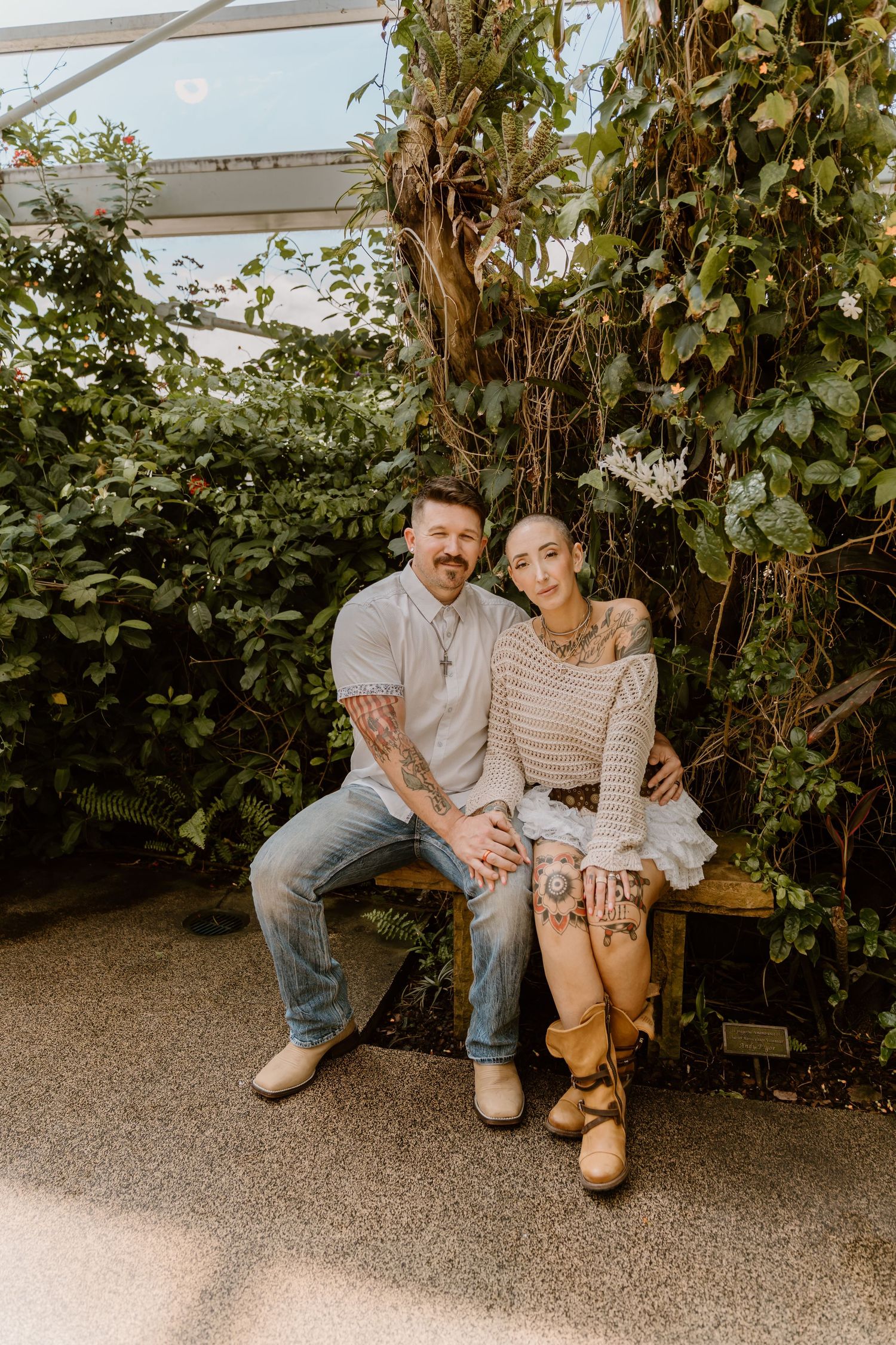 Casual outdoor portrait on bench surrounded by lush green vine covered walls.