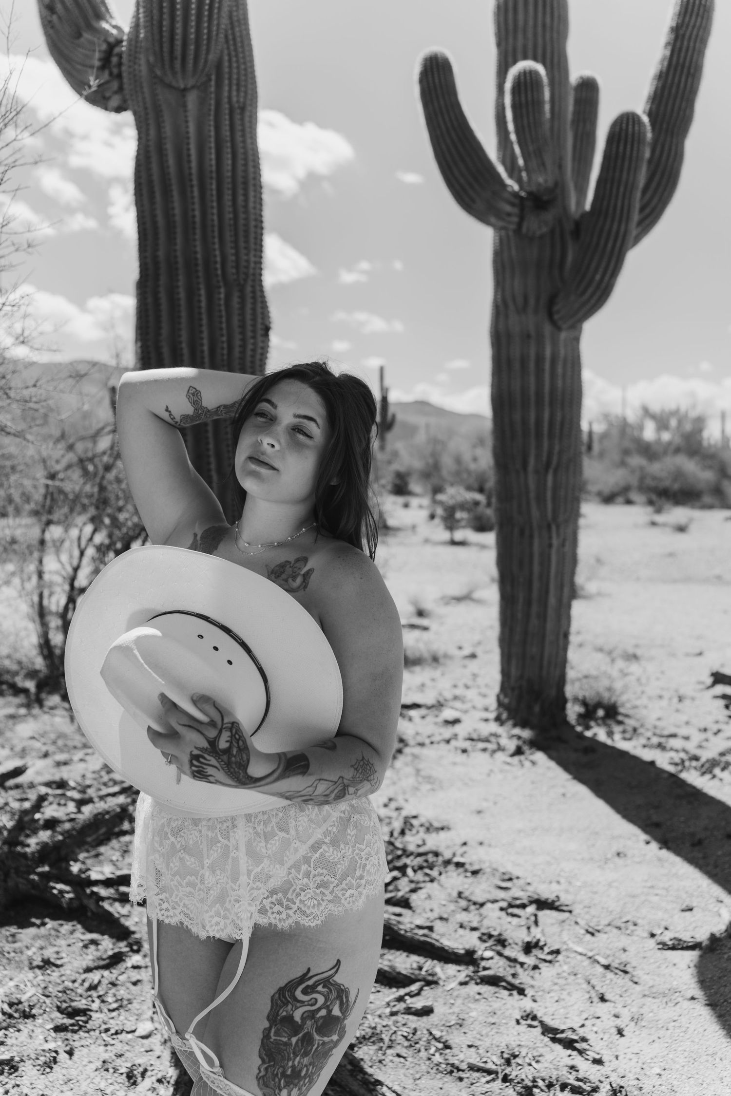 Black and white boudoir desert photoshoot with saguaro cacti in a stark landscape.