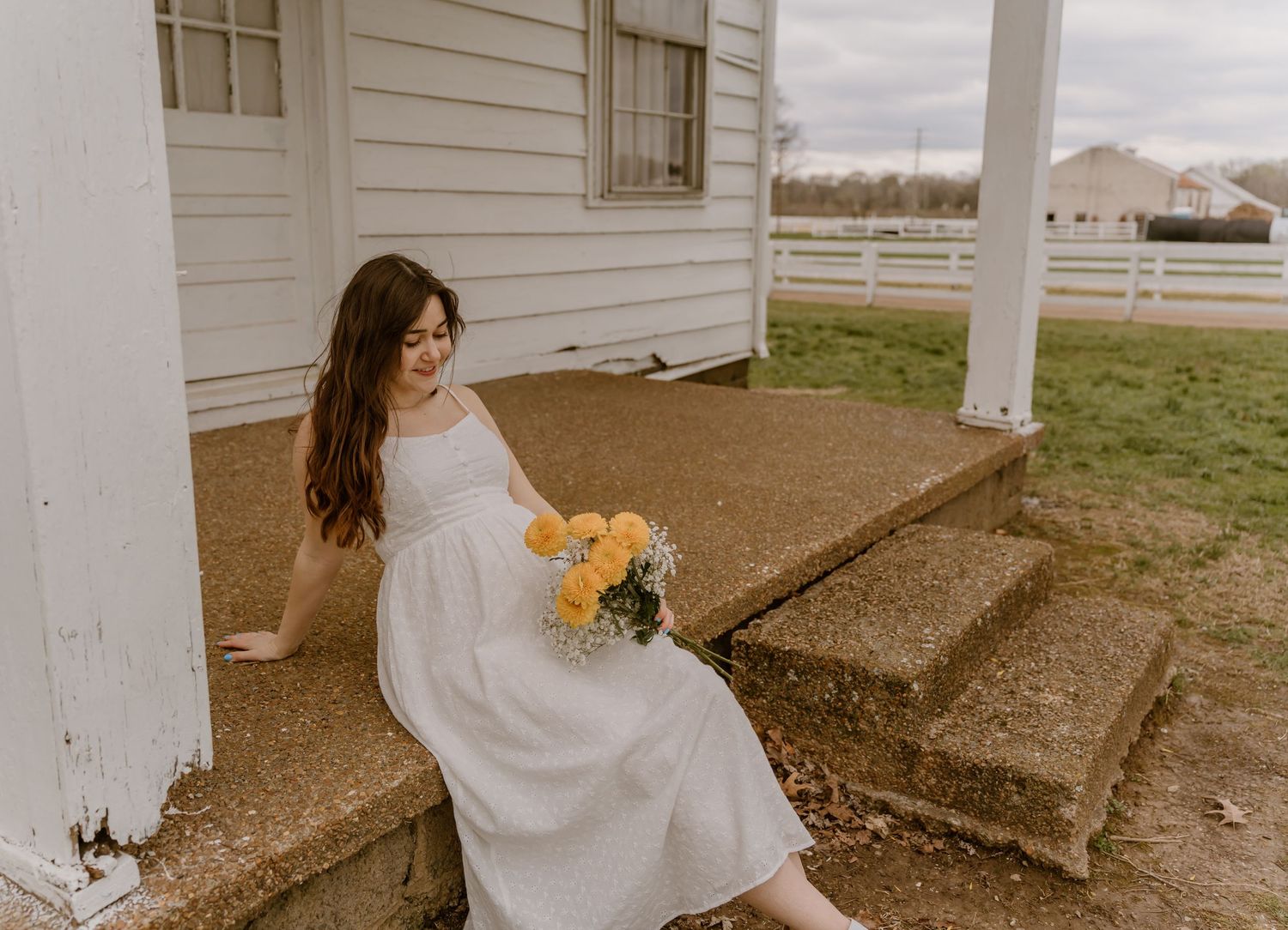 Person in white dress sitting on concrete steps outside a white building on an overcast day.