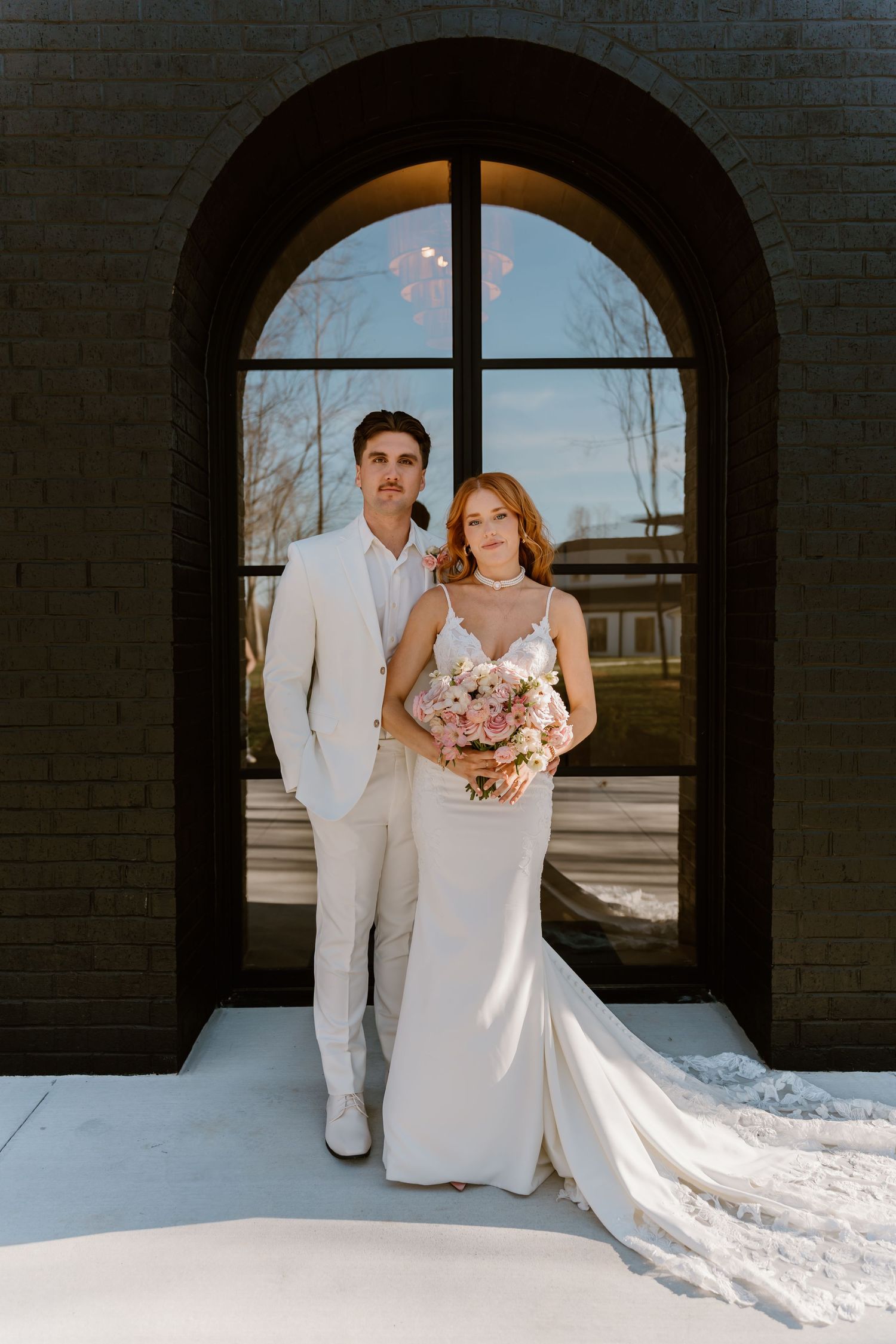 A wedding couple poses dramatically against black brick walls and arched windows.