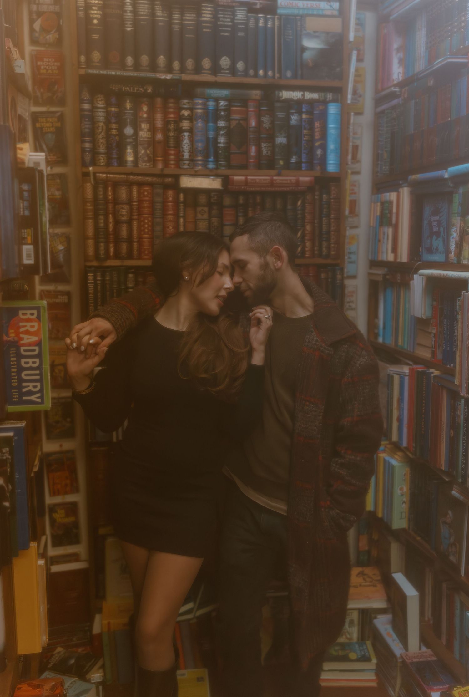 Someone browses through books in a dimly lit library aisle filled with wooden shelves and hardcover volumes.