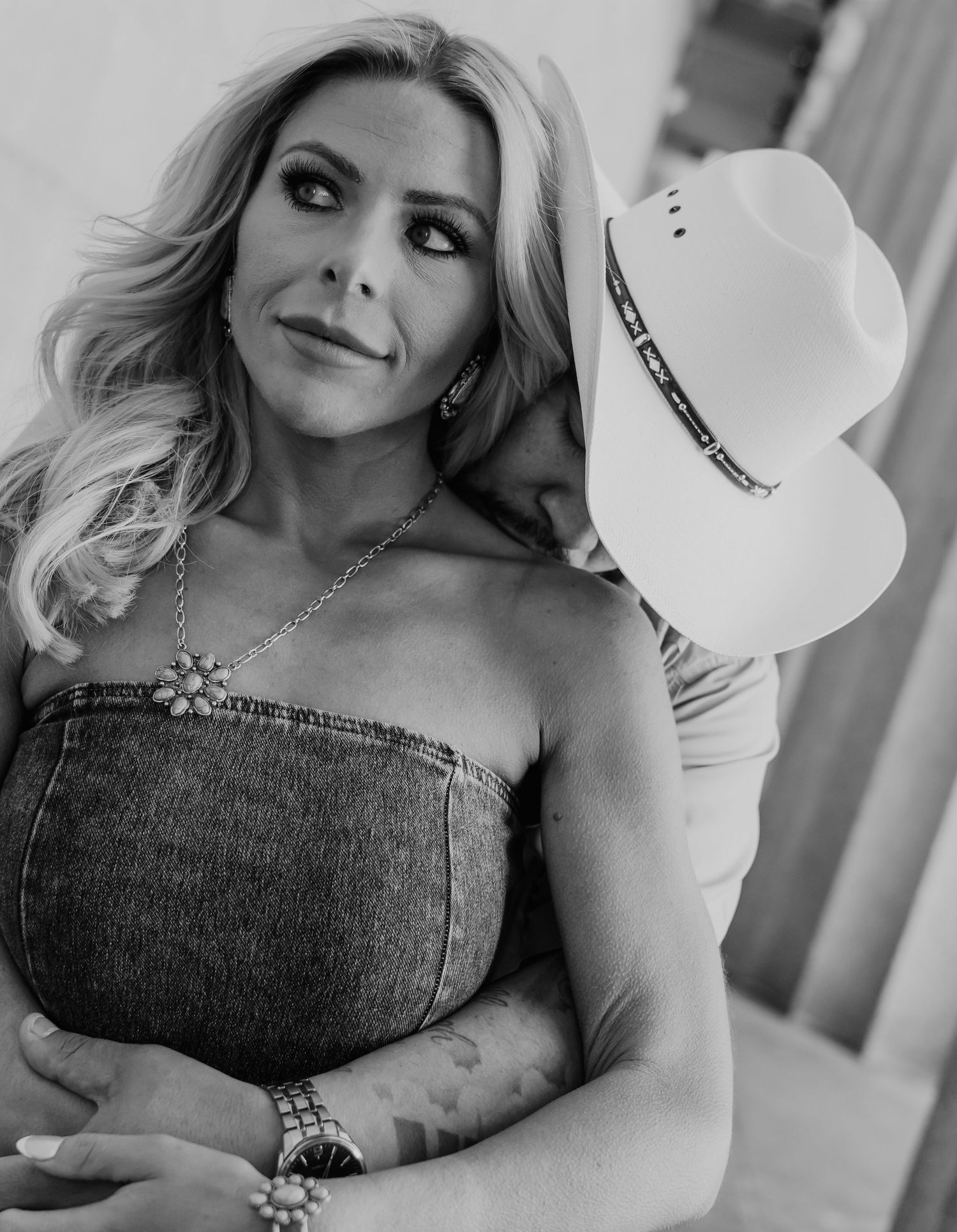 Black and white portrait of a woman in a denim dress holding a white cowboy hat.