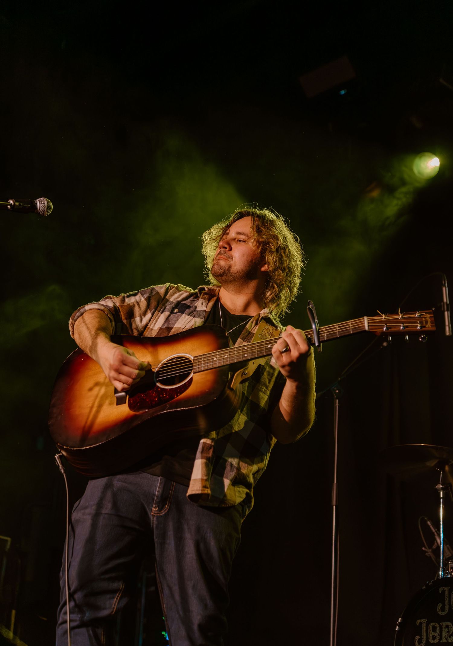 A musician performs on an acoustic guitar on a dimly lit stage during a concert performance.