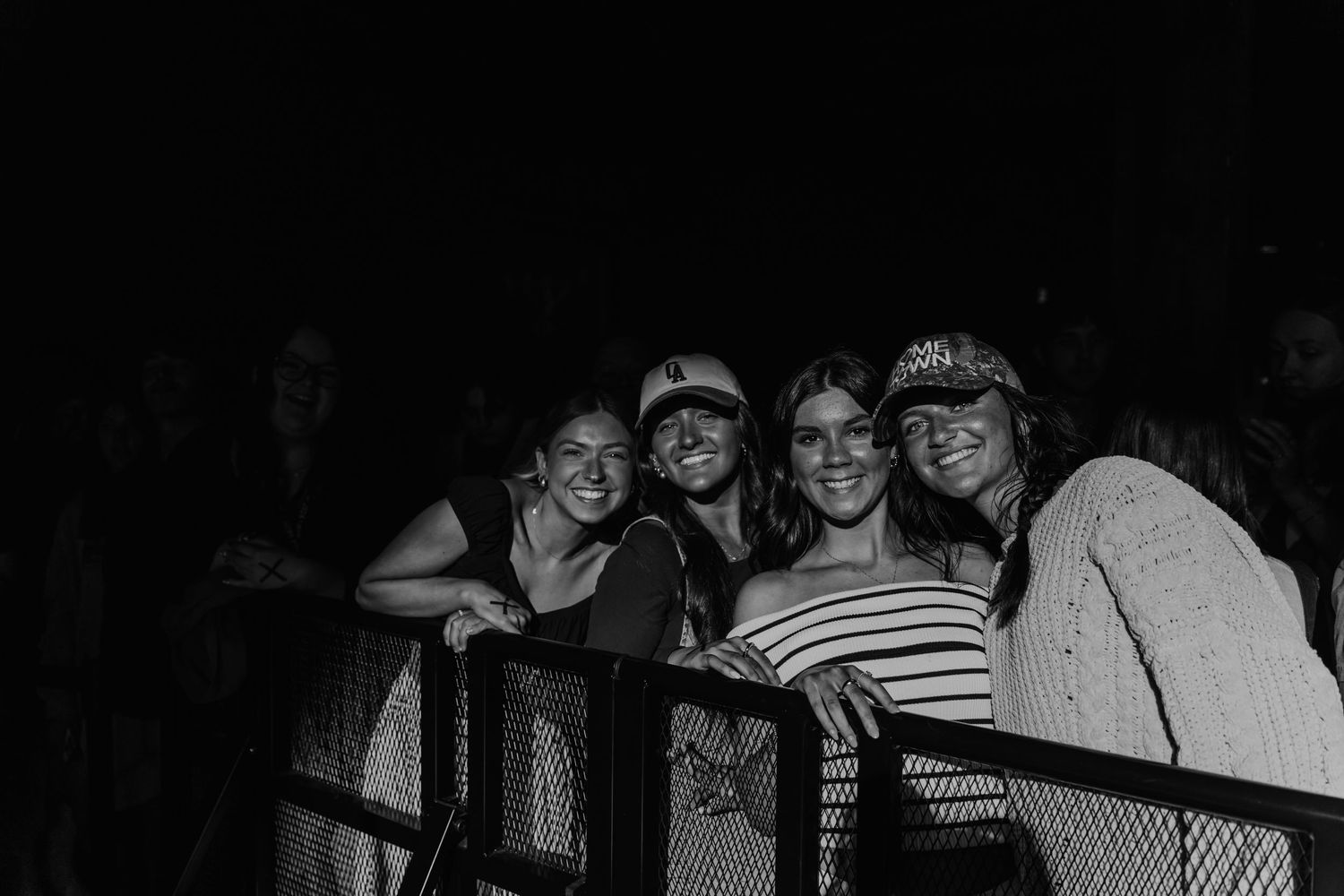 Black and white photo of fans leaning on railing at concert venue.