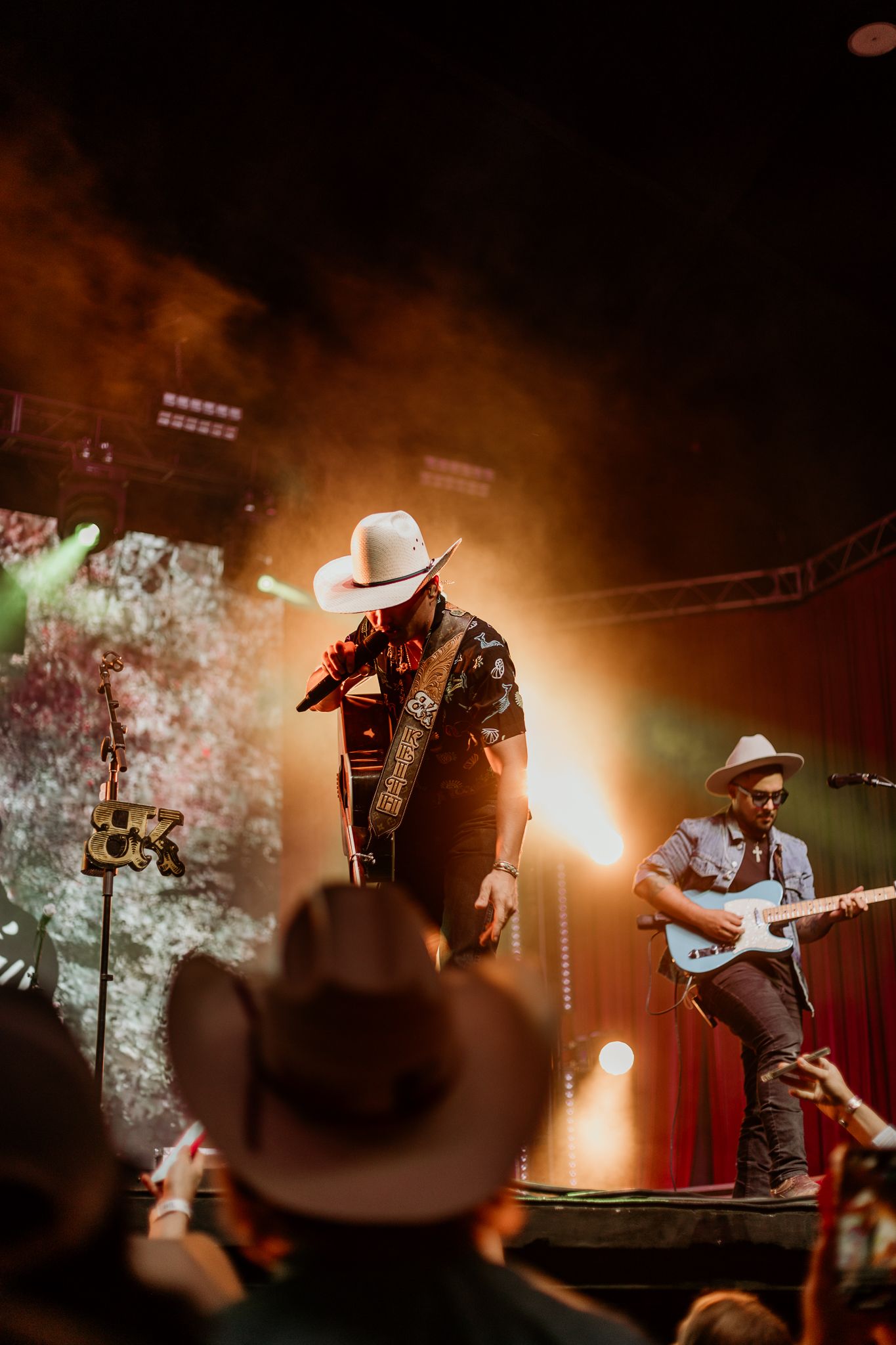 Band members performing with cowboy hats under warm amber stage lighting during concert.