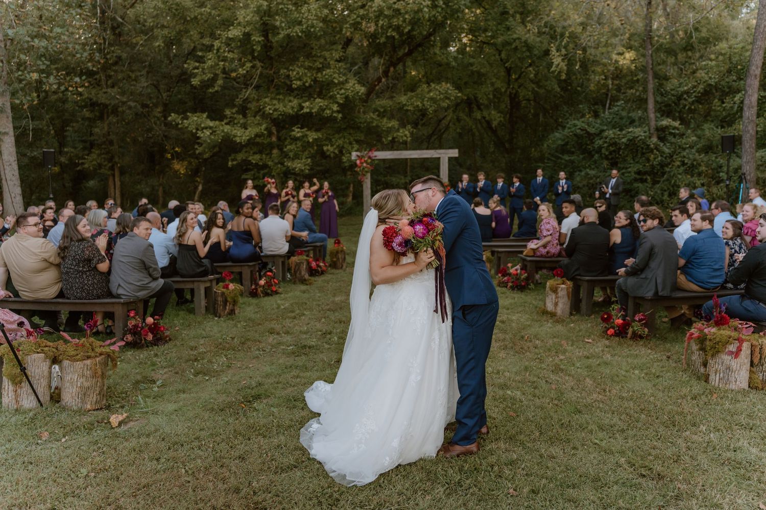 Outdoor wedding ceremony in a grassy field with wooden bench seating and guests gathered to celebrate in Tennessee.