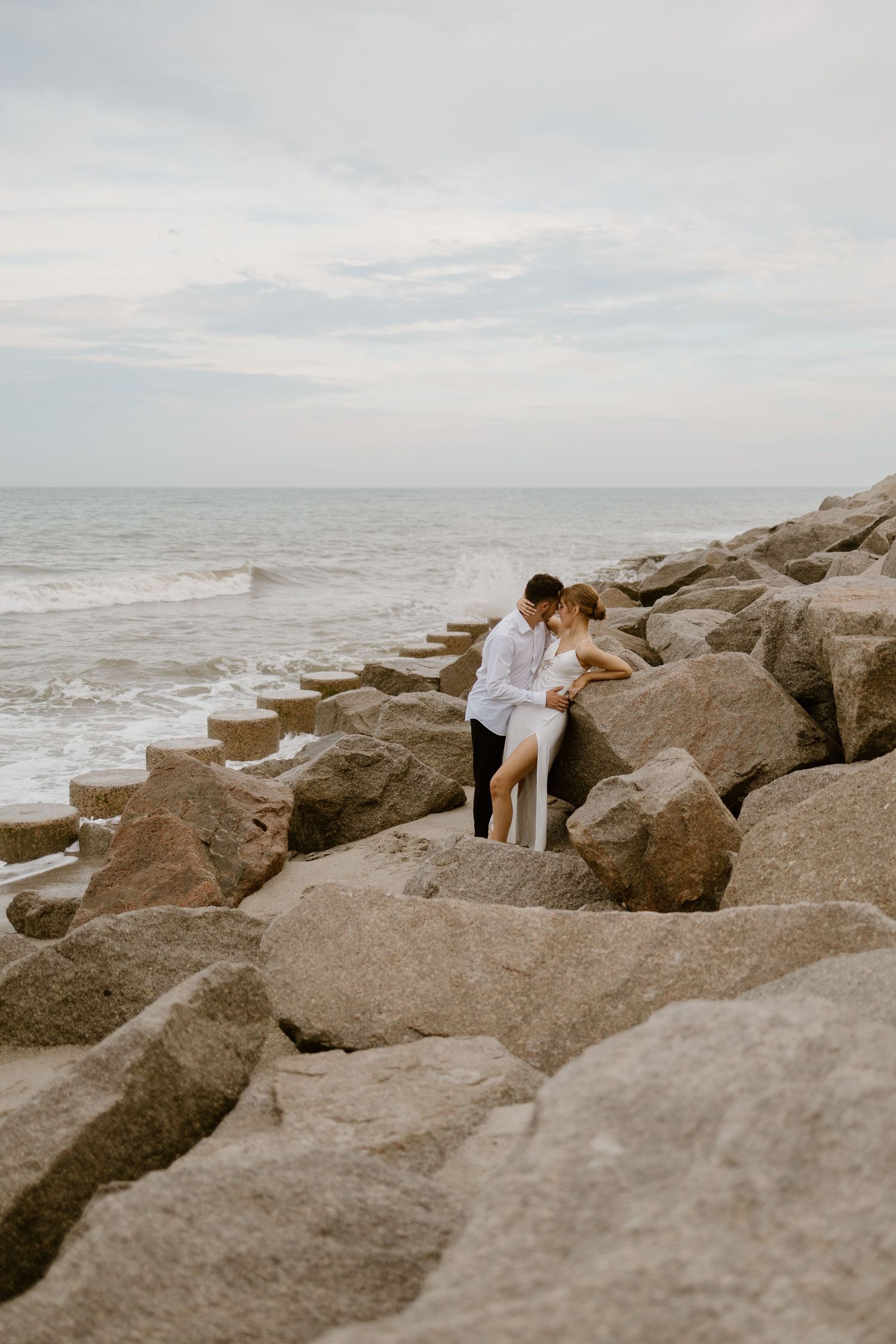 A romantic moment on coastal rocks with crashing waves in the background.