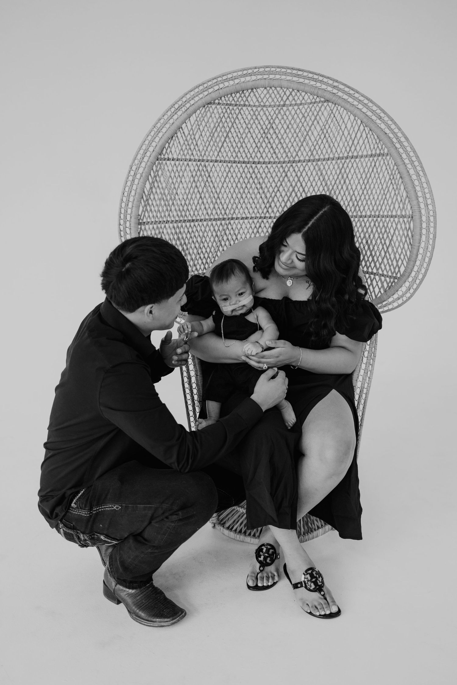 A family shares an intimate moment while seated in a peacock chair against a grey background.