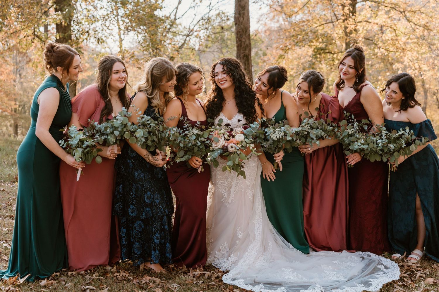 Wedding party in burgundy and green dresses poses together in autumn setting.