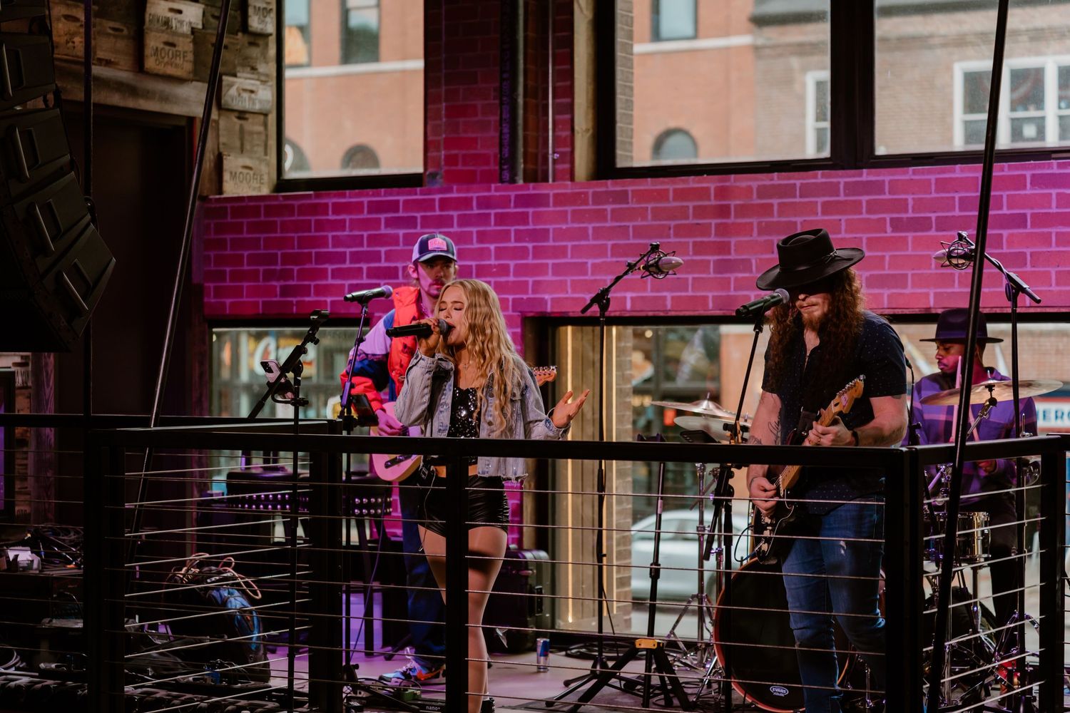 Live band performing on stage with pink brick wall backdrop at an indoor venue.