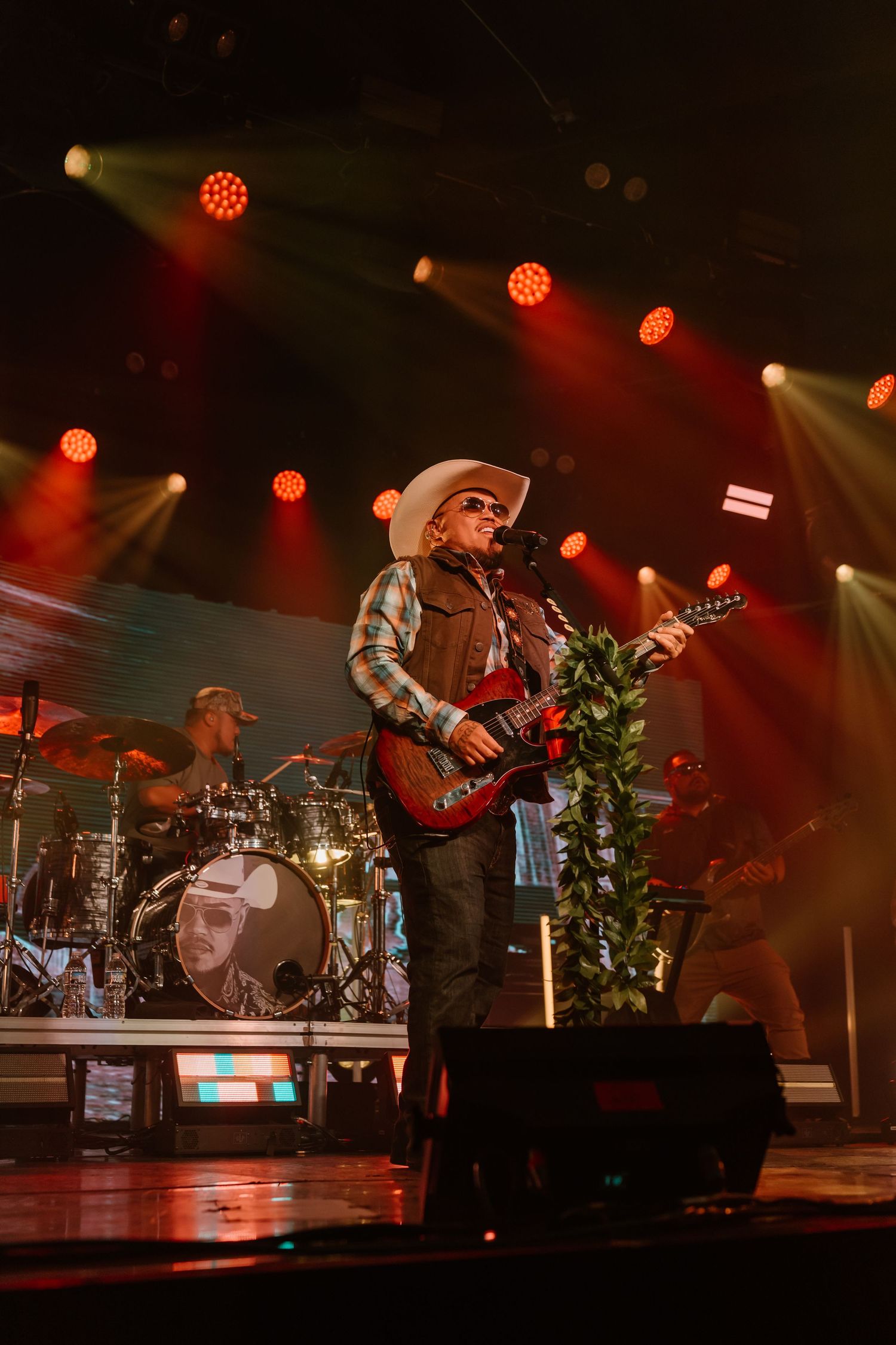 Band performs on stage with red lighting and concert equipment visible in the background.
