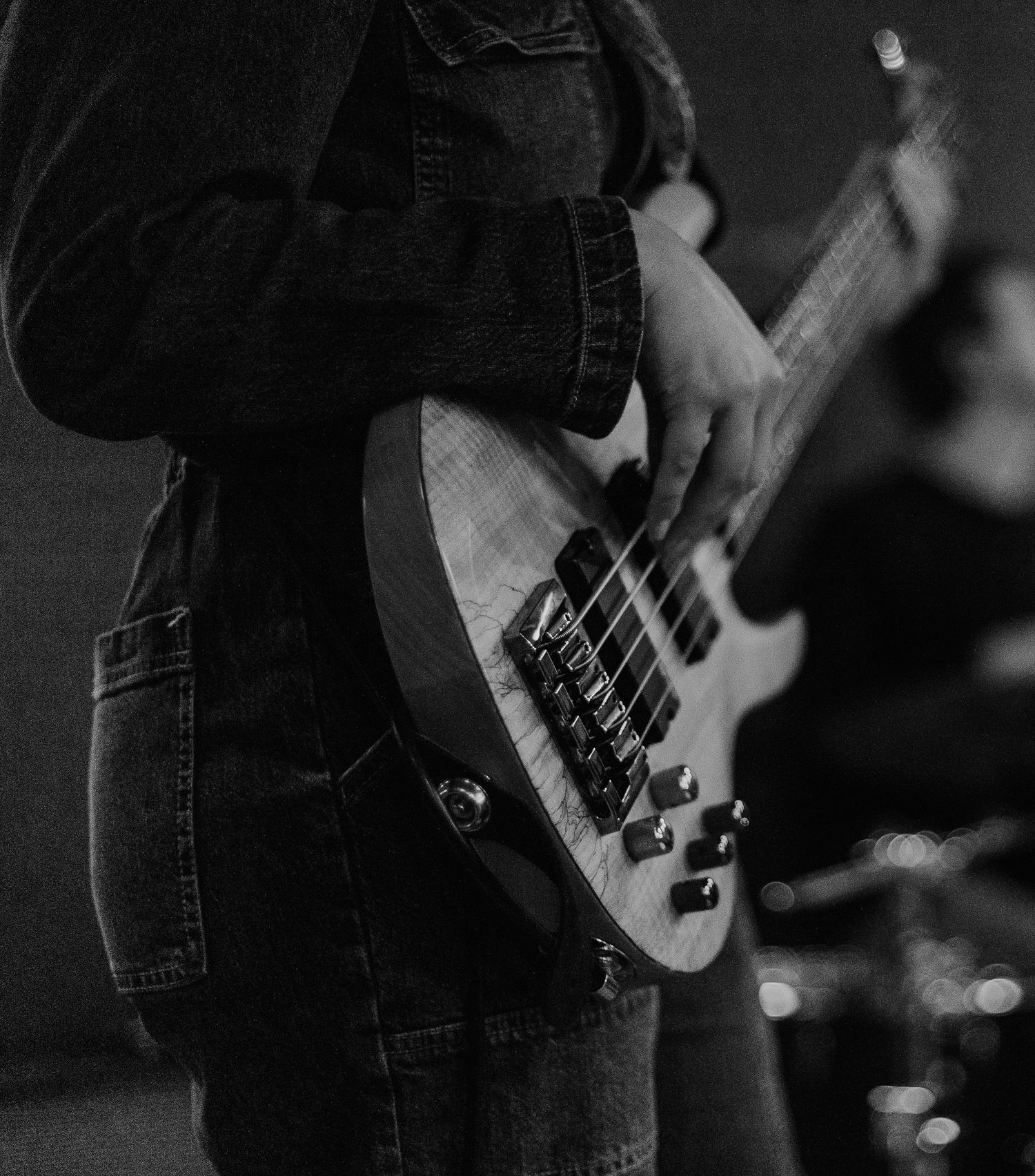 Close-up shot of musician playing bass guitar during a dark concert performance.