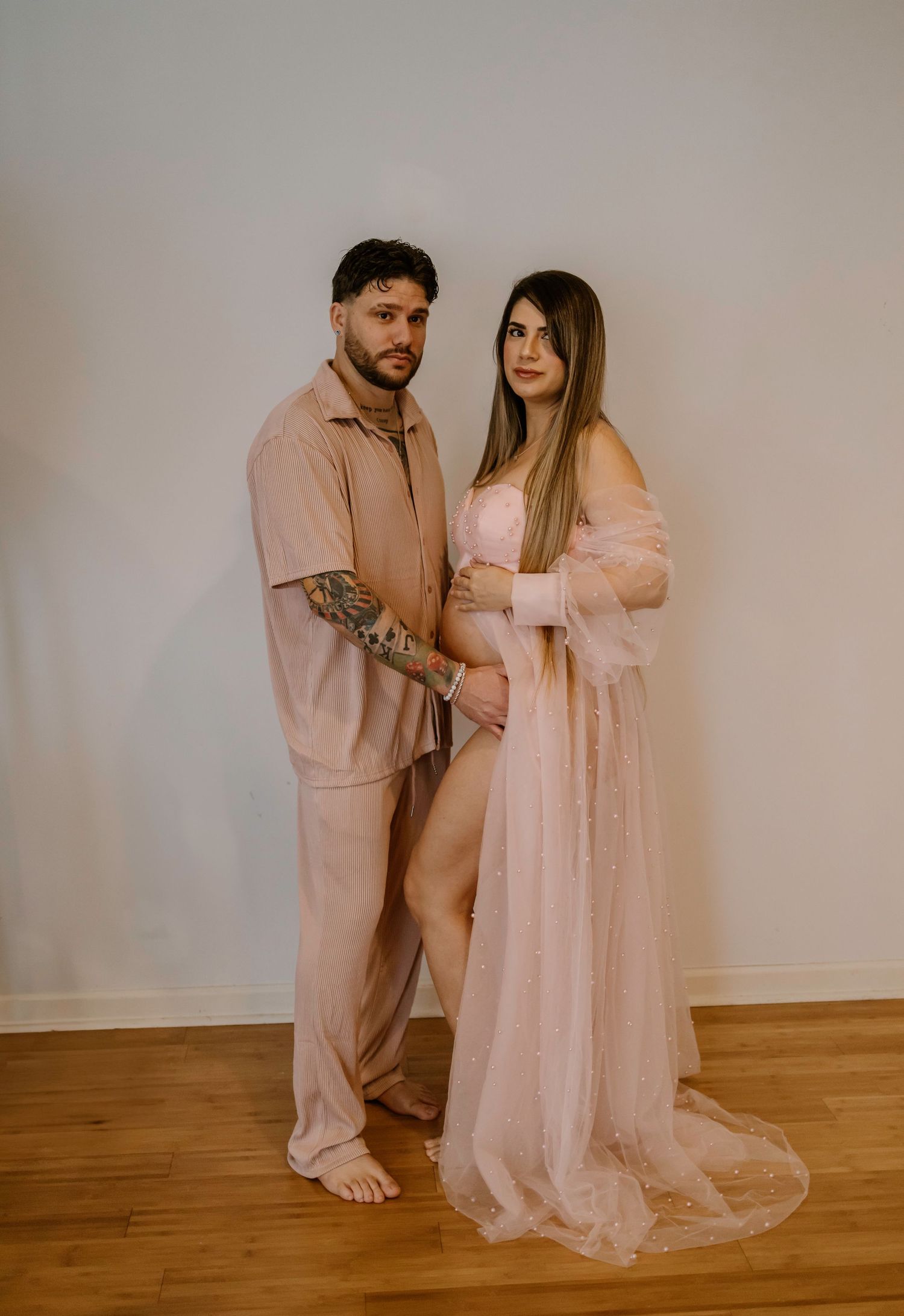 A couple poses in matching pink loungewear against a neutral wall in a minimalist setting.
