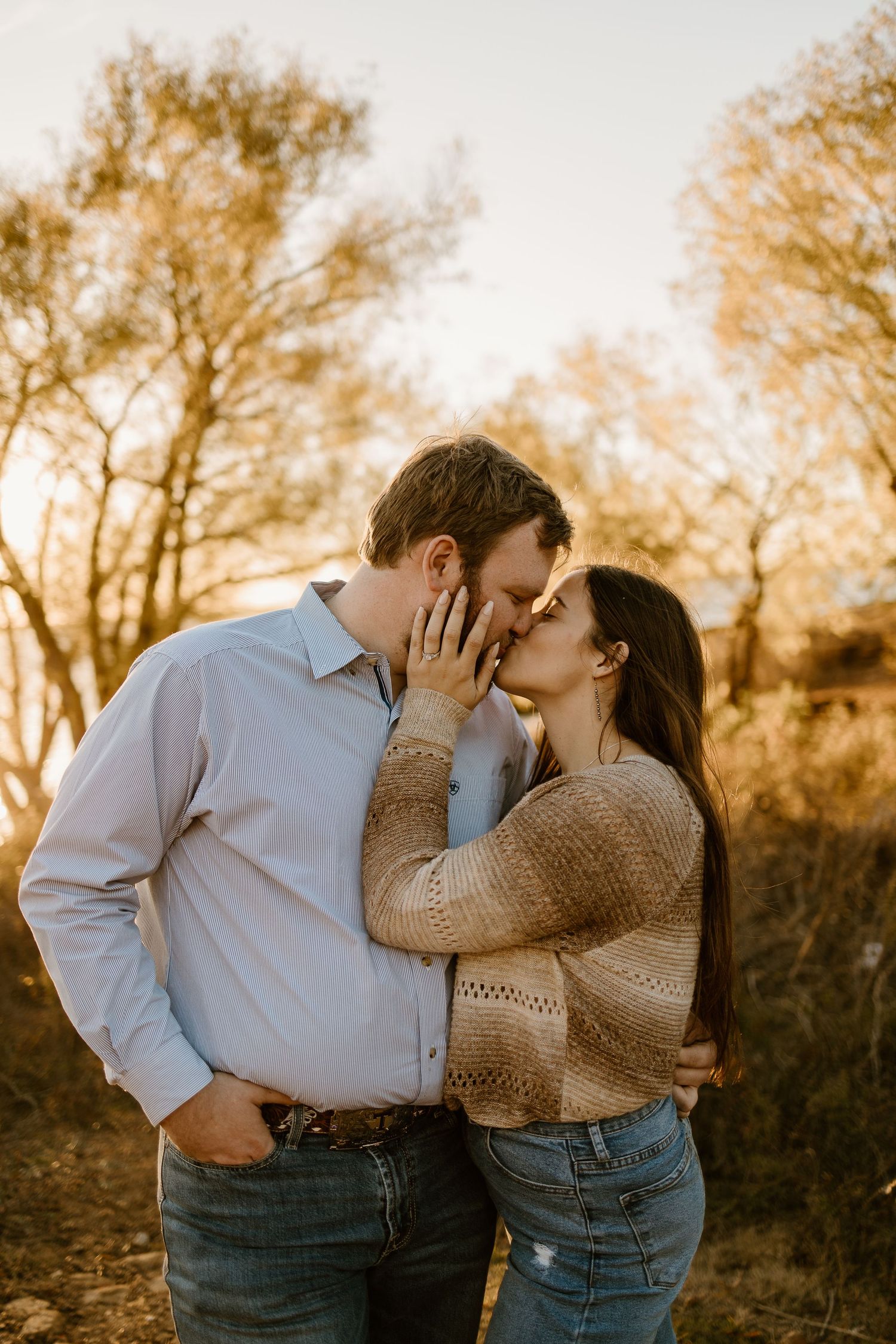 A couple shares an intimate moment during golden hour with autumn trees in the background.