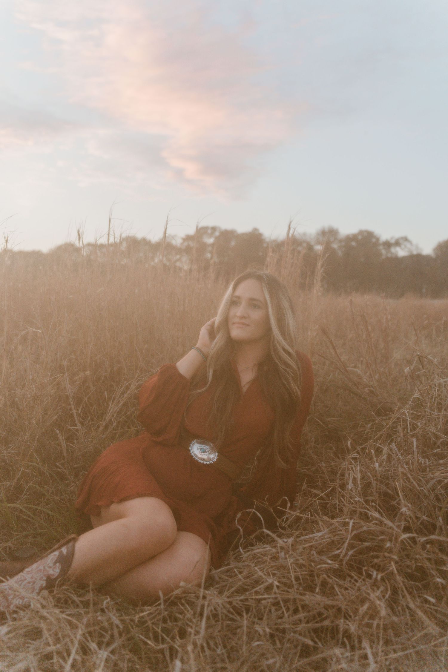 A person in a red sweater poses gracefully in a sunlit field of dried grass during golden hour.