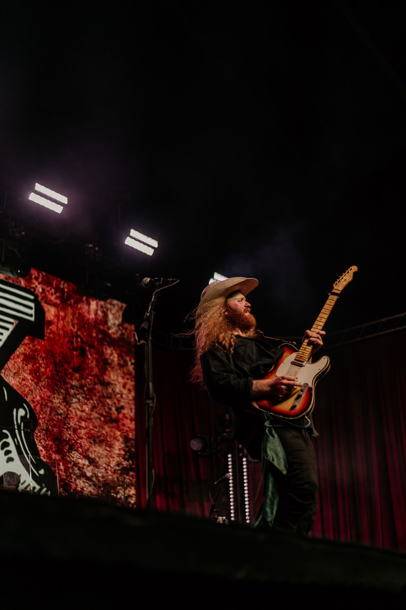 Band members silhouetted against red lighting perform energetically on stage with guitars.