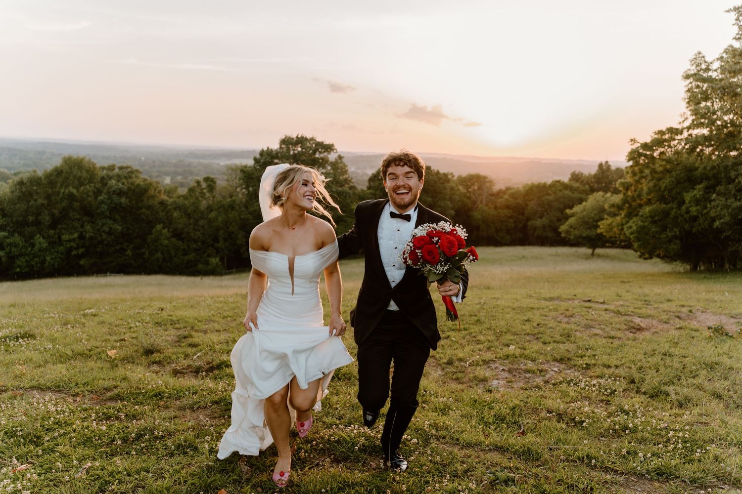 A couple runs together through a sunlit meadow at sunset during their wedding celebration.