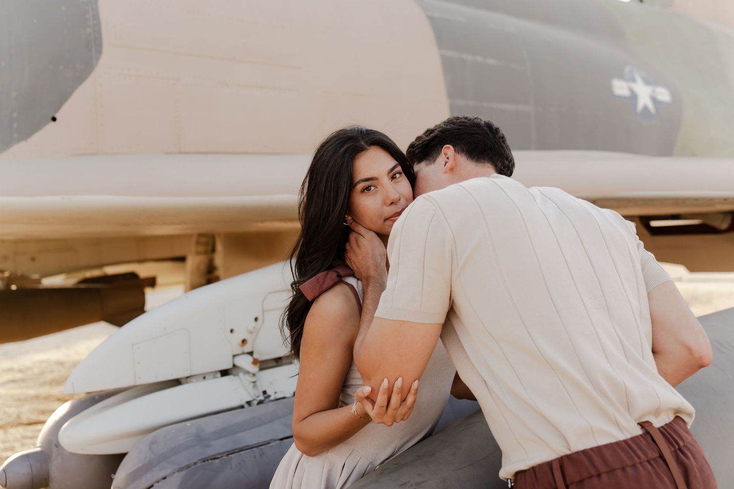 Couple sharing a romantic moment leaning against a vintage military aircraft during an outdoor engagement photo session.