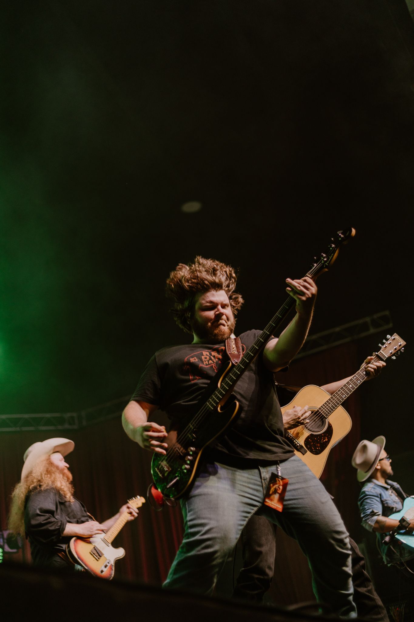 Musicians play guitars under green stage lighting during an intense live performance.