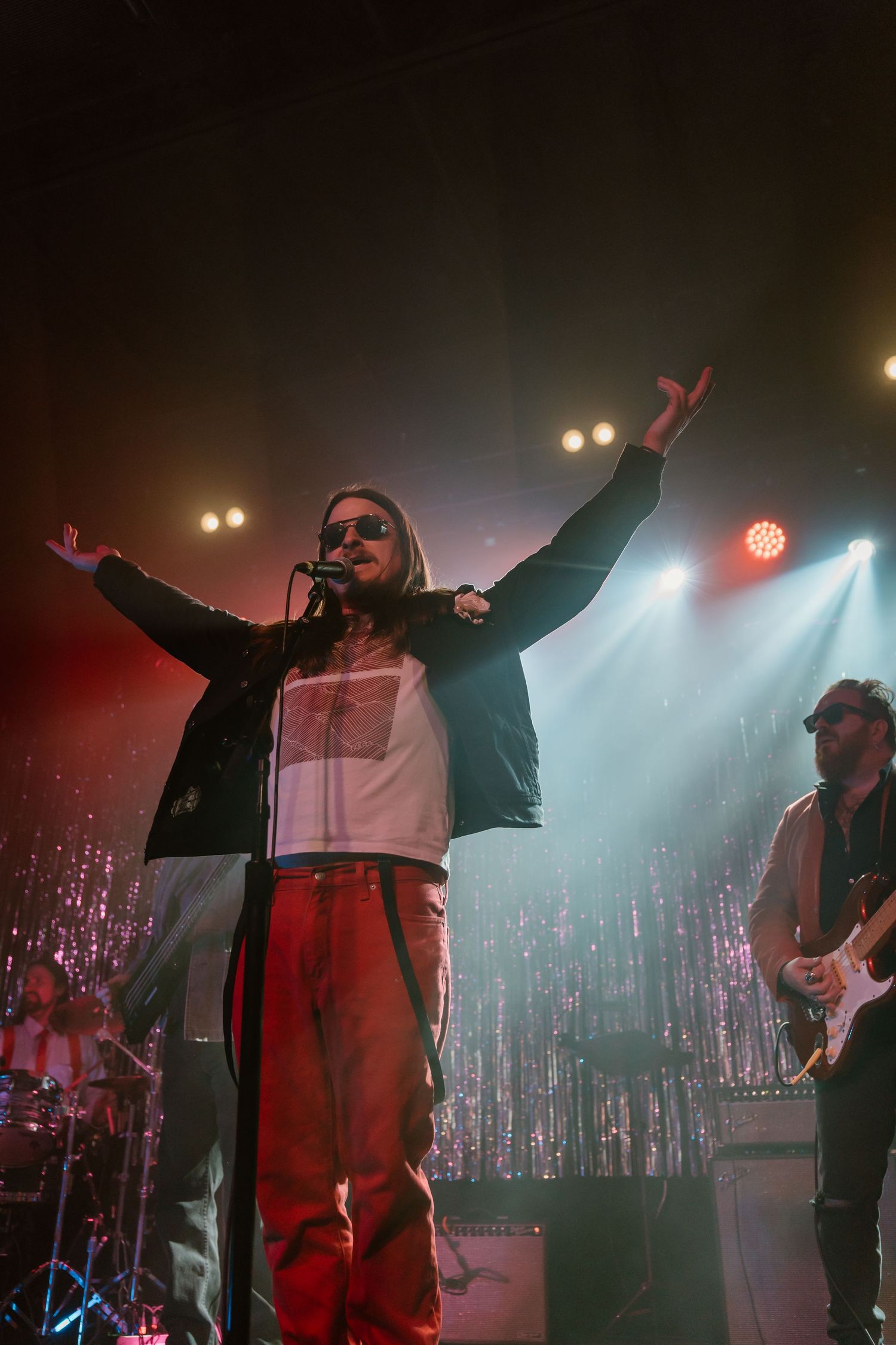 Performers on stage with dramatic lighting and silver tinsel backdrop during an energetic show.