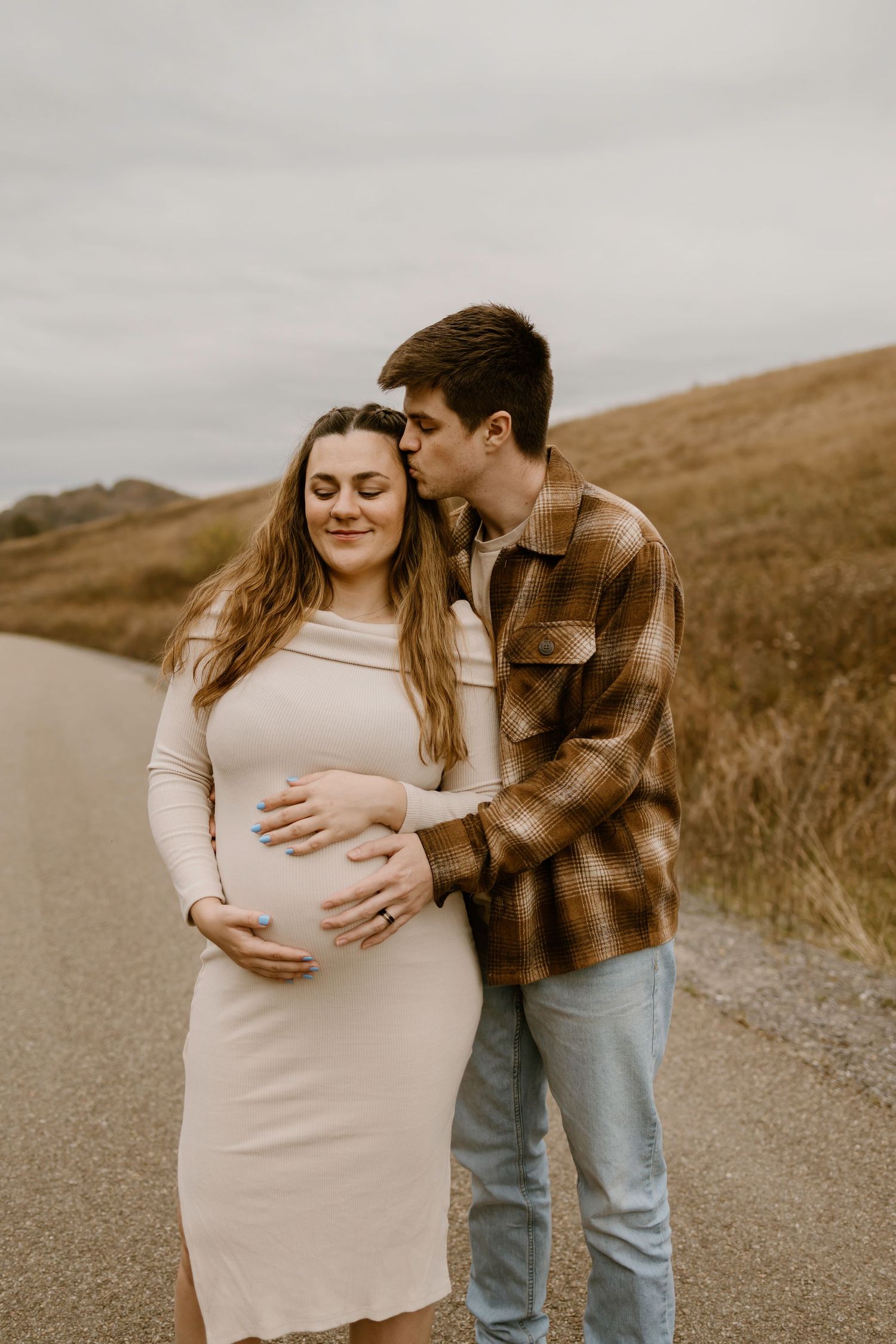 A couple shares an intimate moment on a dirt road during a maternity photoshoot.