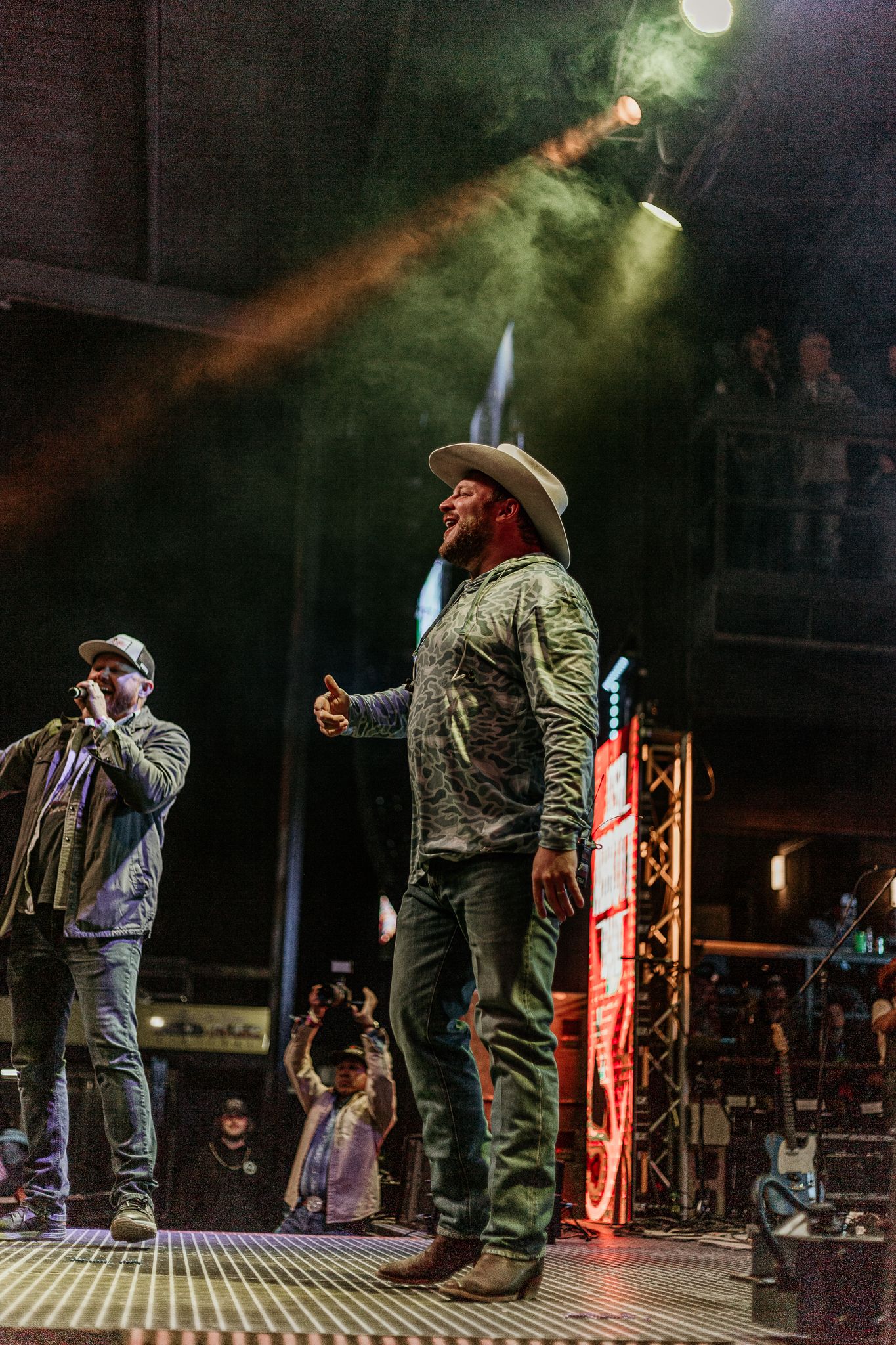 Concert performers in casual attire illuminated by stage lights and red accents during live show.