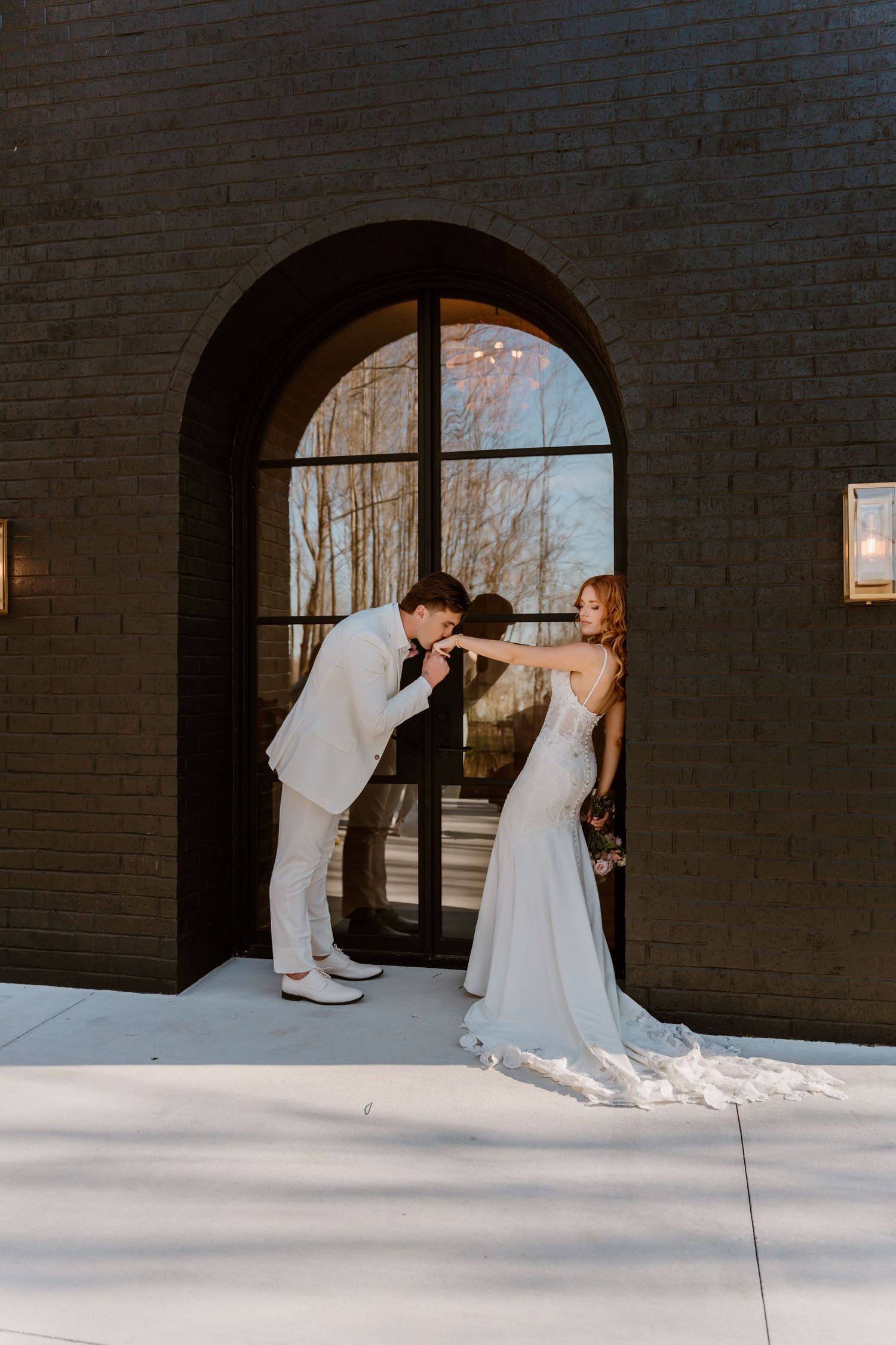 A couple shares intimate dance moments in front of arched windows and brick walls.