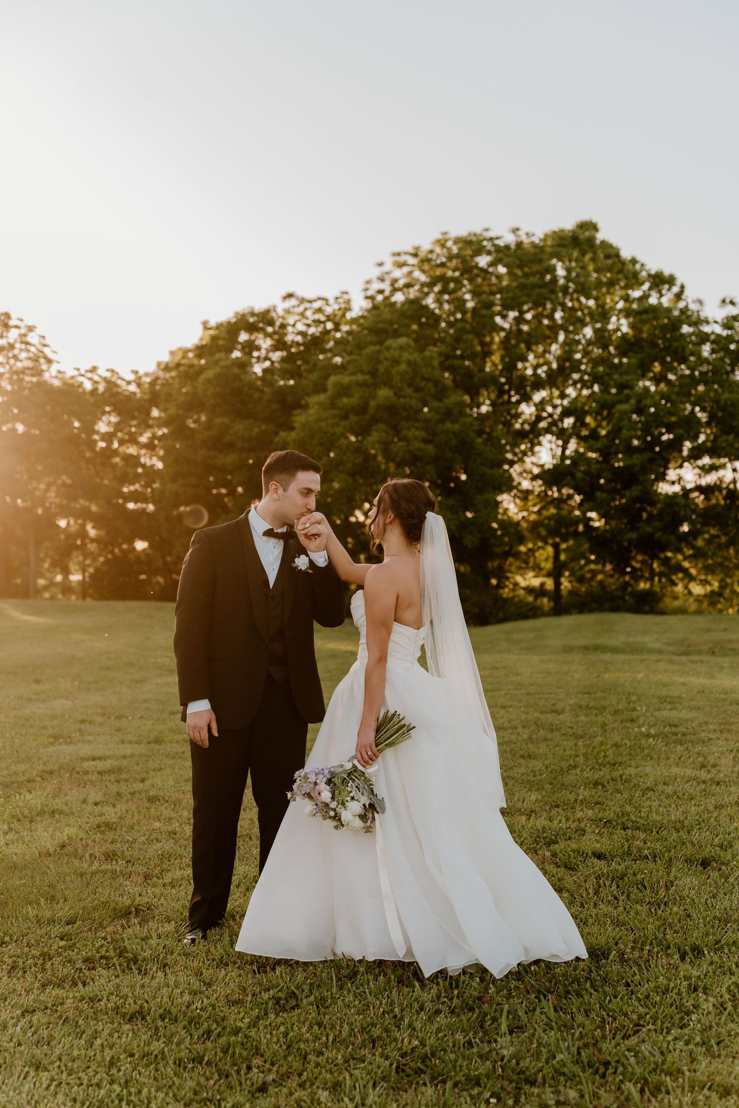 A wedding couple shares an intimate moment in a sunlit meadow at golden hour.