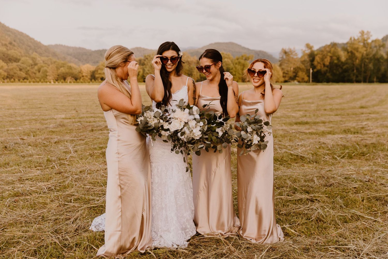 Wedding party in blush pink dresses stands together in a sunlit field.