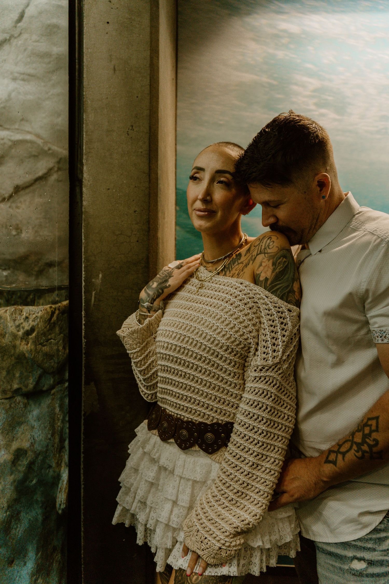 Intimate portrait showing tender embrace against textured wall in warm lighting.