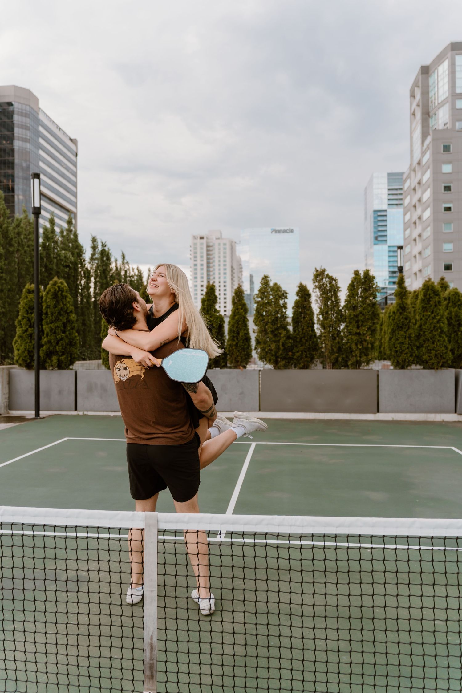 A sequence of four shots showing a tennis player stretching and warming up on an outdoor court with city buildings in background.