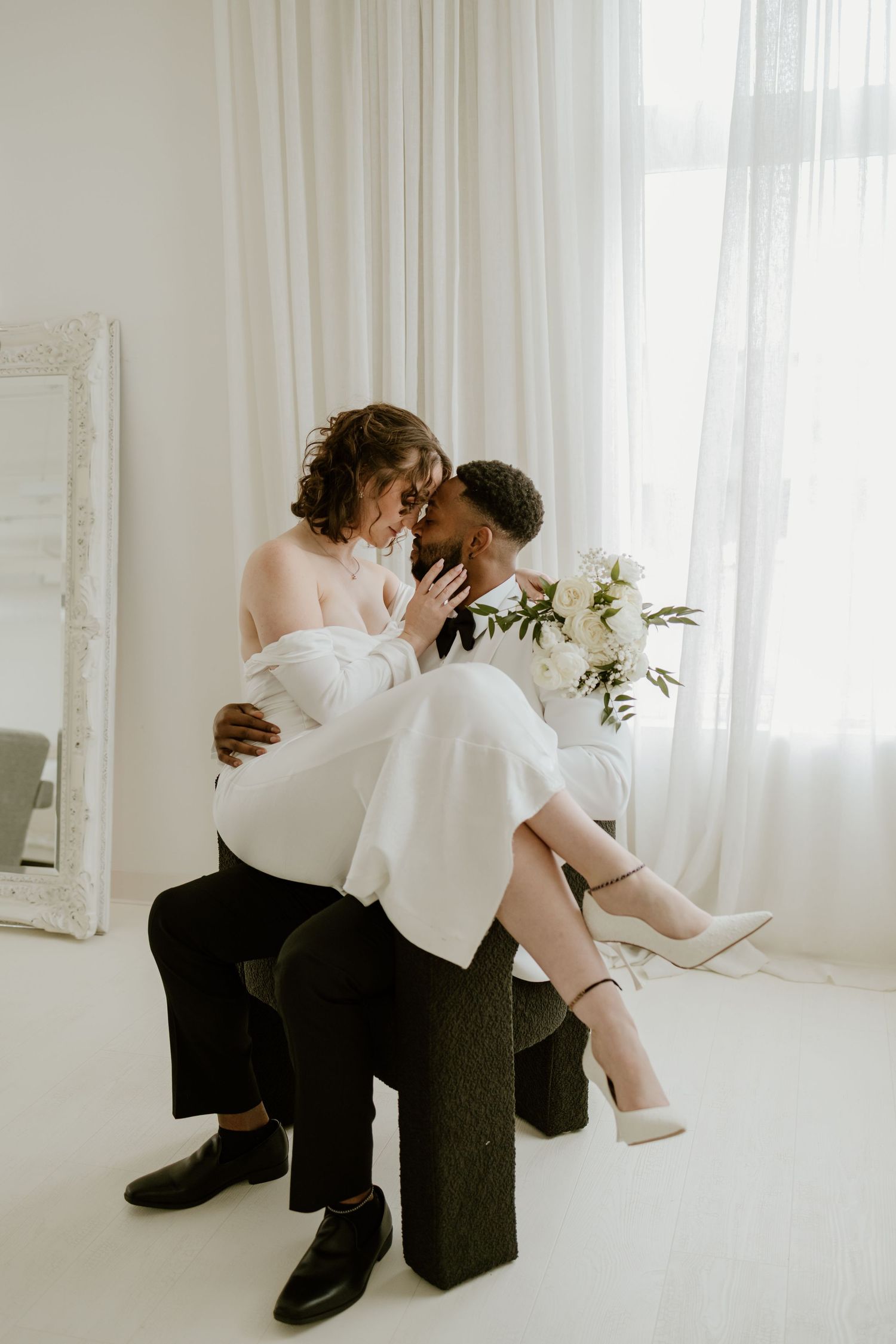 Artistic black and white photo series showing tender moments between a couple in a bright white room with sheer curtains.