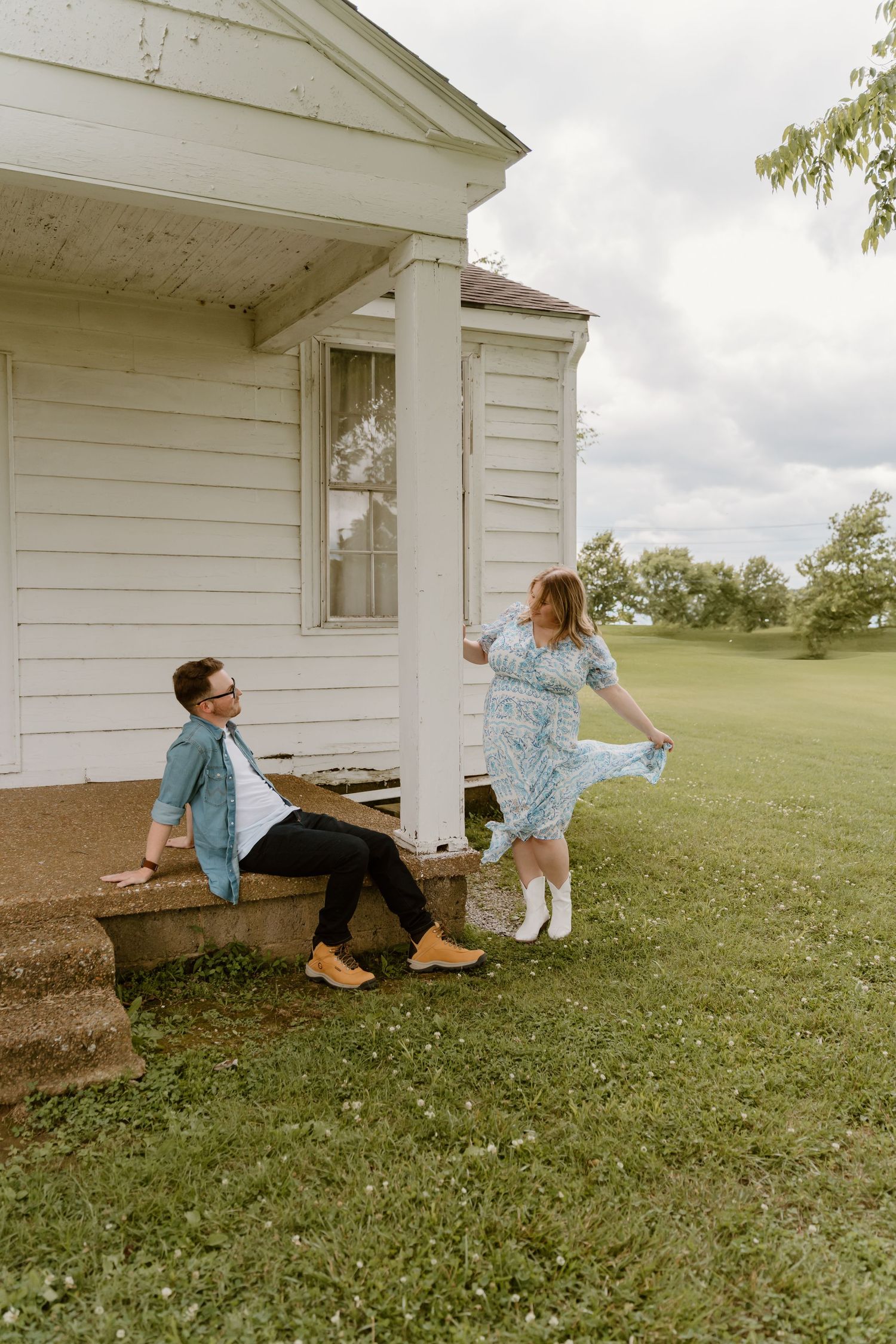 A playful moment captured outside a white farmhouse with a couple enjoying time on the porch steps.