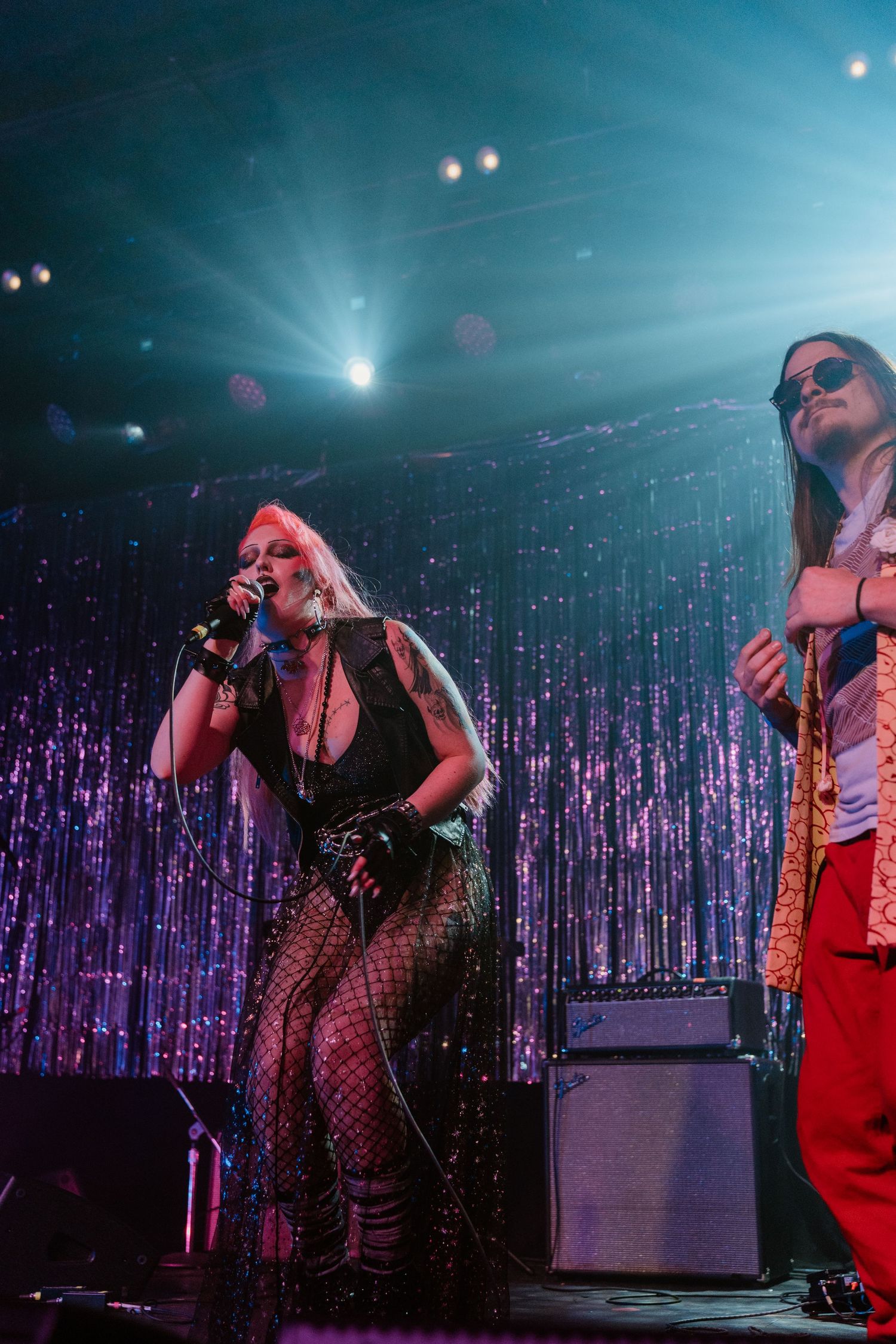 Performers on stage with dramatic purple lighting and sparkly backdrop during a live music show.