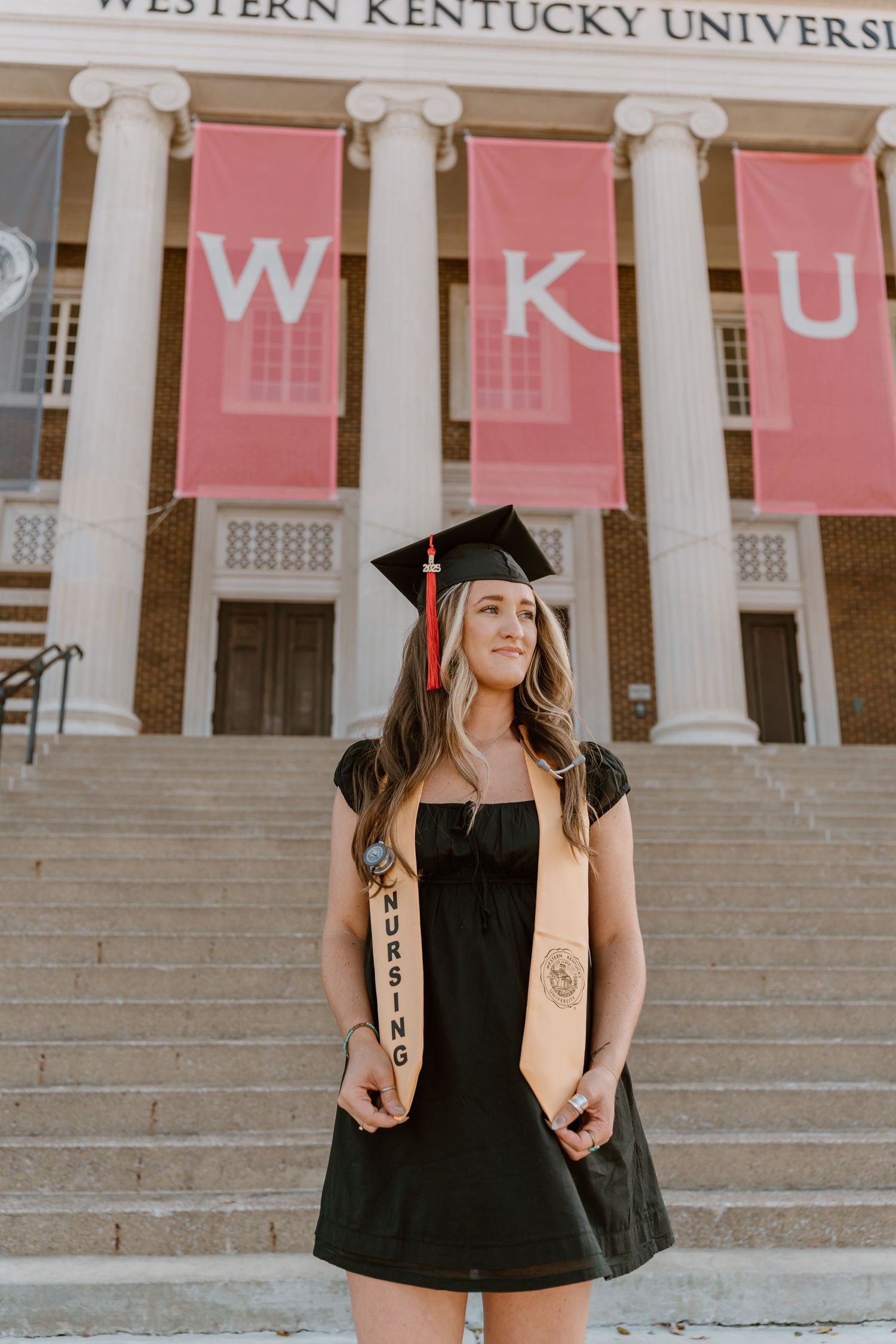 Graduate poses in front of Western Kentucky University columns wearing cap and gown.