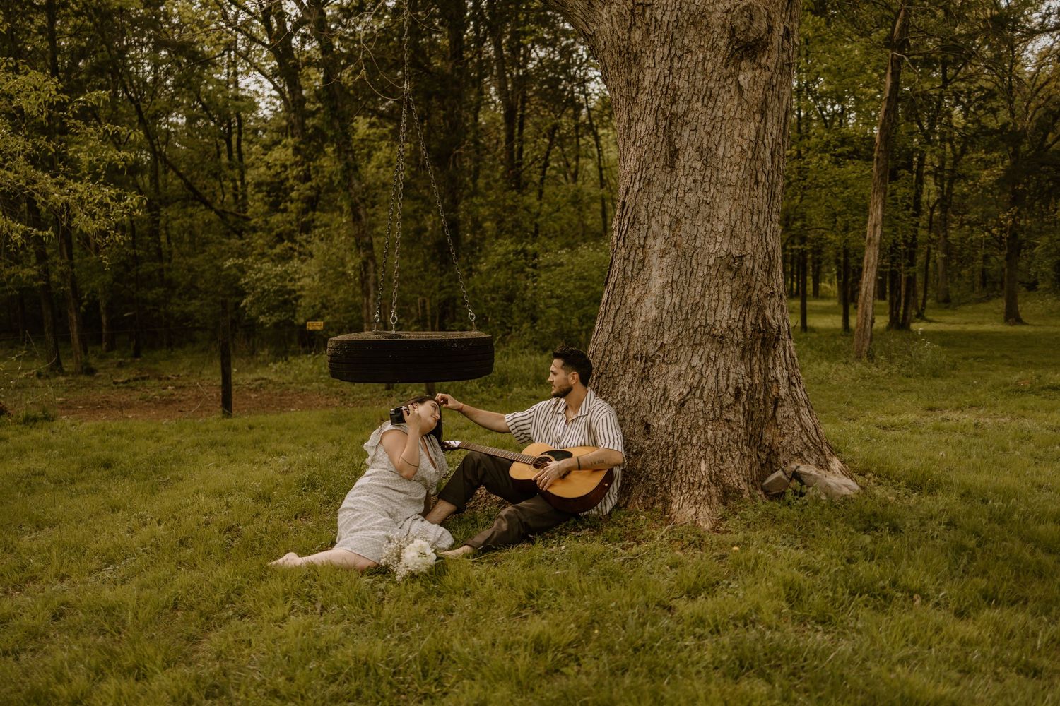 Couple enjoys intimate moment under large tree in wooded park setting in Tennessee.